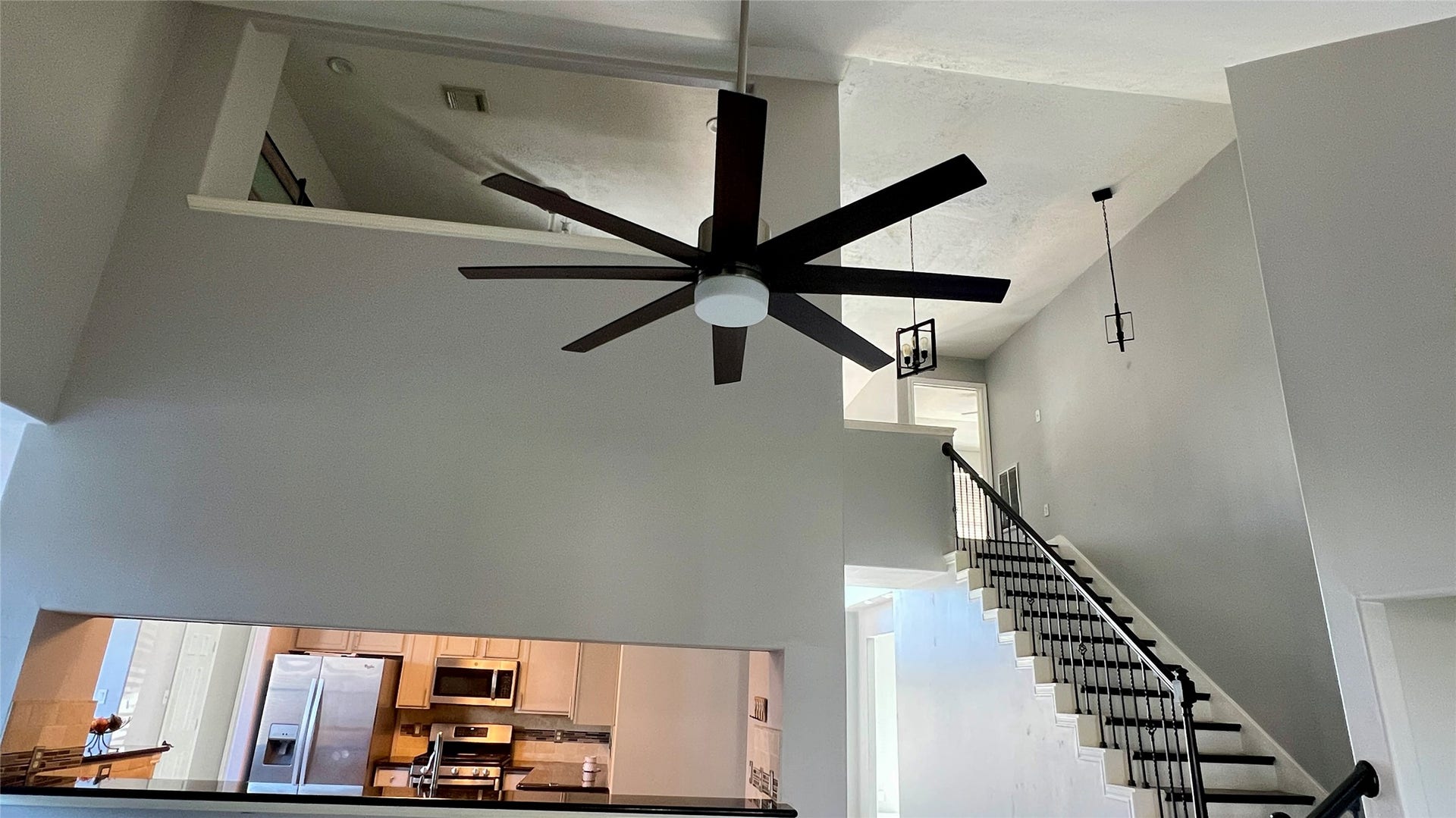 open-concept home interior with high ceilings. Large ceiling fan The kitchen is visible, featuring stainless steel appliances and a contemporary design.