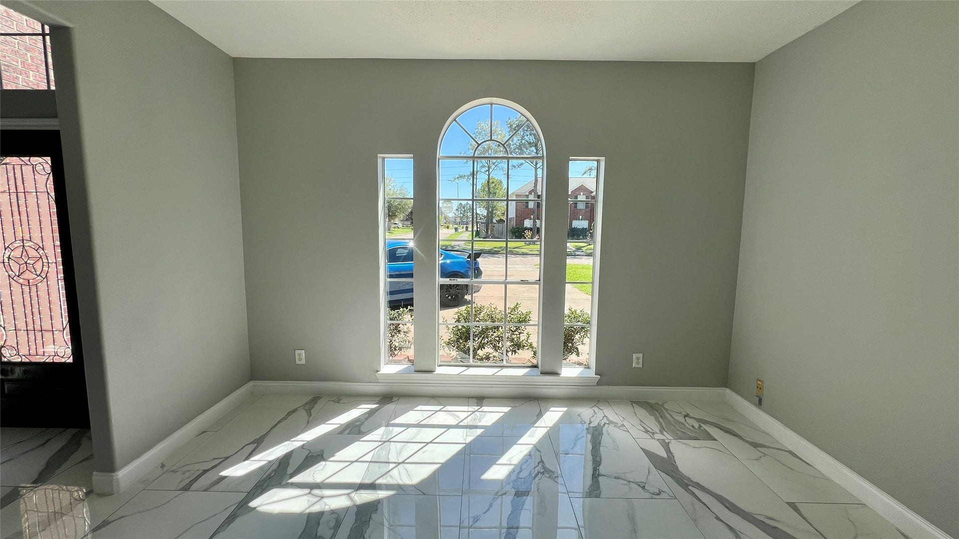 Bright room with large arched window, gray walls, and glossy marble-patterned tile flooring with plenty of natural light.