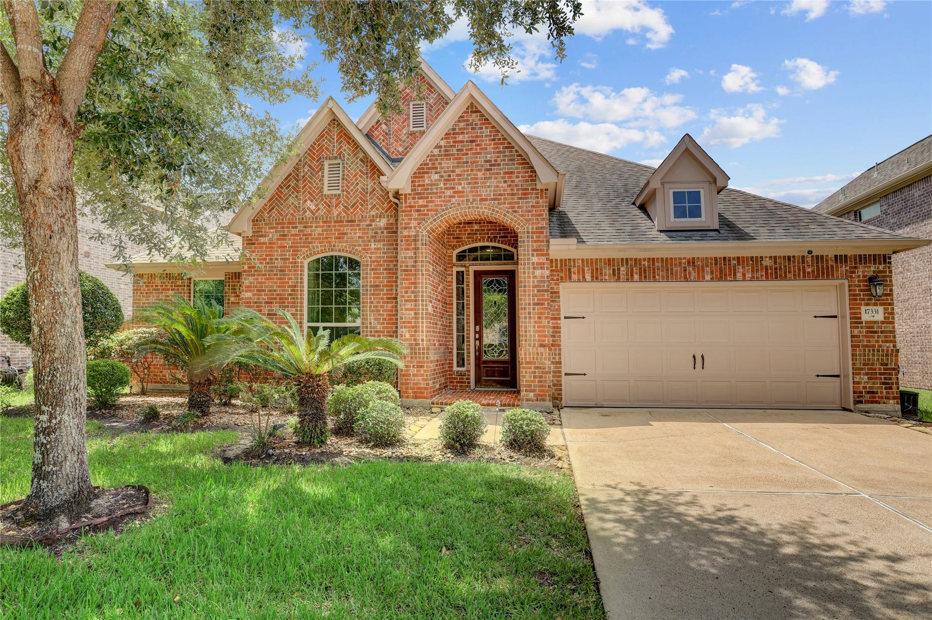 Inviting brick exterior showcases timeless curb appeal with manicured landscaping, a covered entry framed by a striking arched brick faade, and an attached two-car garage.