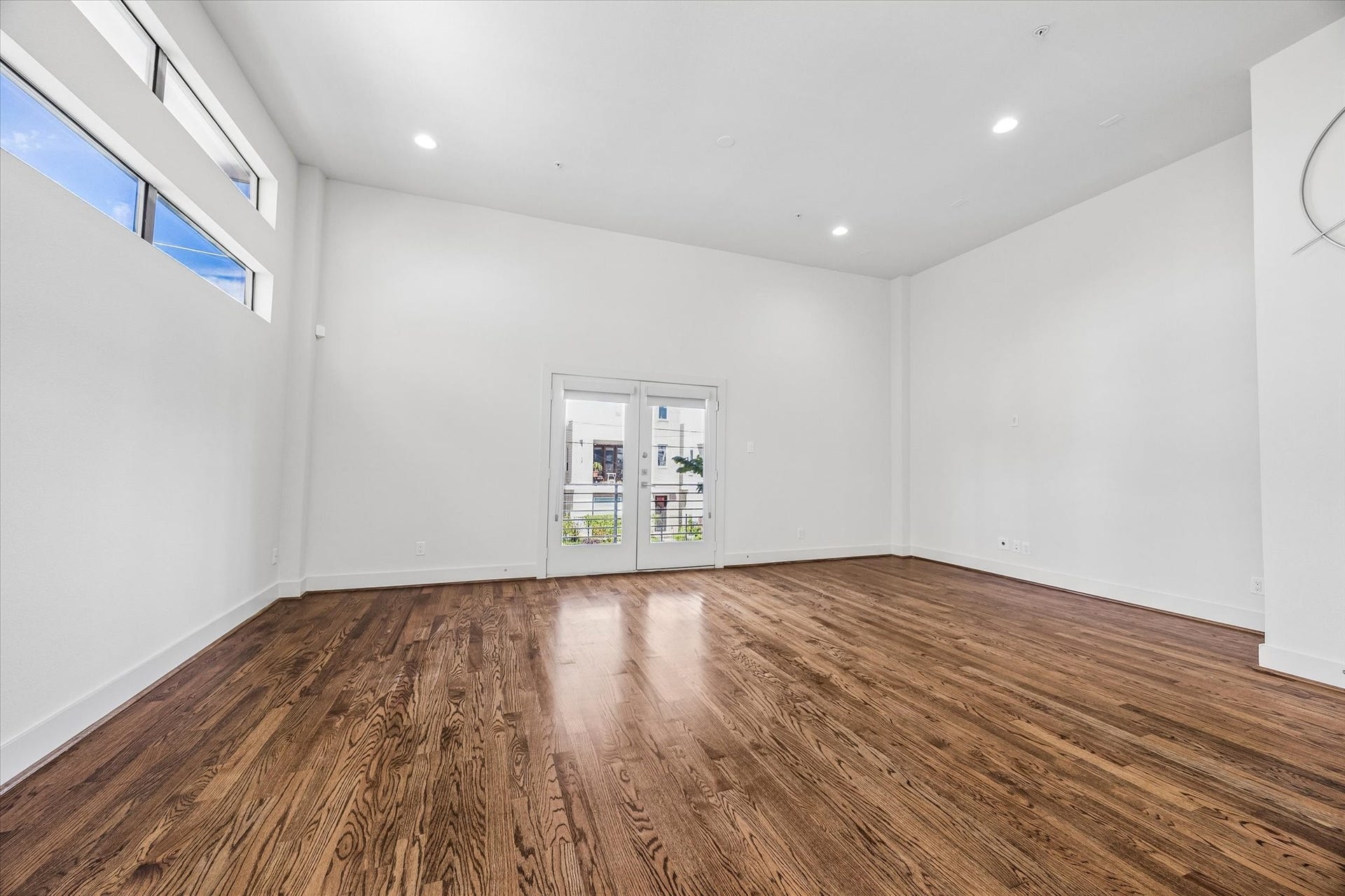 1215 Summer Street, #A, Houston, TX 77007 Spacious living area with high ceilings, wood flooring, recessed lighting, and large windows. French doors provide access to the balcony.