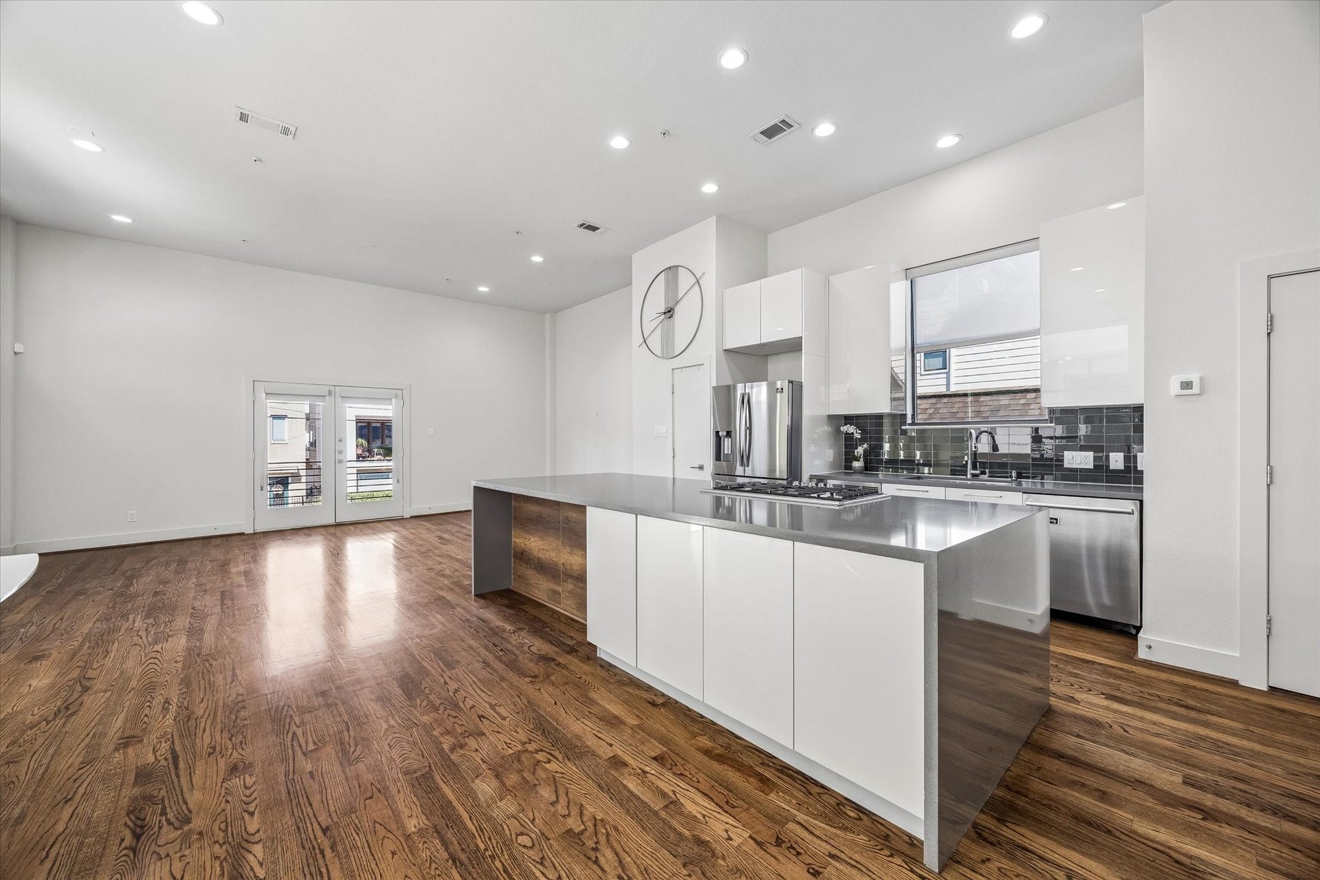 1215 Summer Street, #A, Houston, TX 77007 Kitchen overlooking the living area, featuring a large island with a gas cooktop, sleek white cabinetry, stainless steel appliances, and a contrasting tile backsplash.