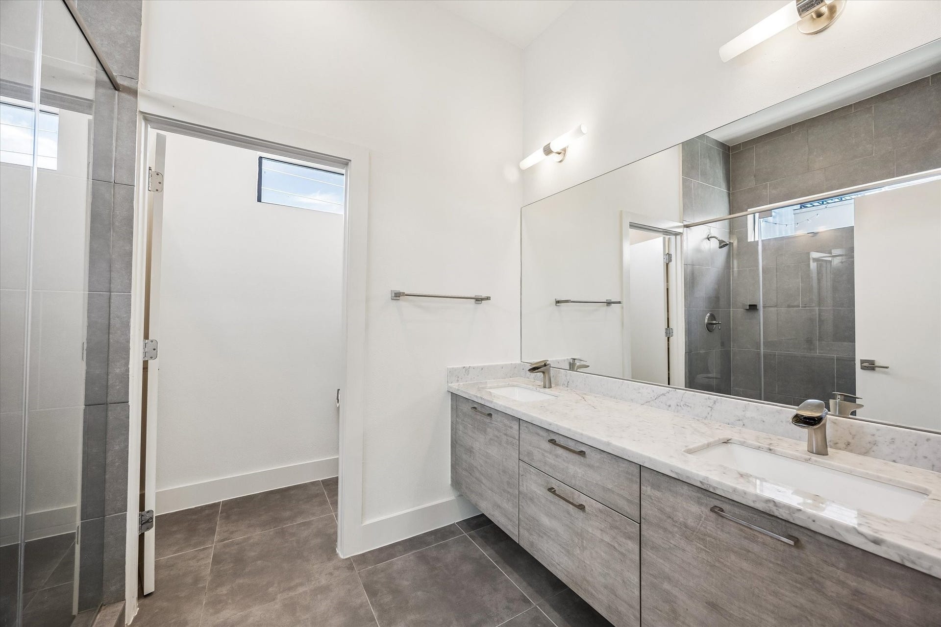 1215 Summer Street, #A, Houston, TX 77007 Primary bathroom featuring a spacious double-sink vanity, a broad mirror, tile flooring, and a glass-enclosed shower with full-height tile.
