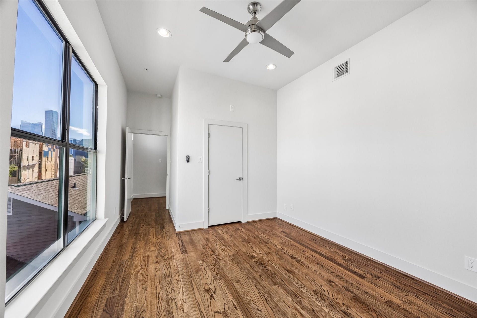 1215 Summer Street, #A, Houston, TX 77007 Alternate bedroom view showcasing the large window with a glimpse of the city skyline, along with wood flooring, a ceiling fan, and closet access.