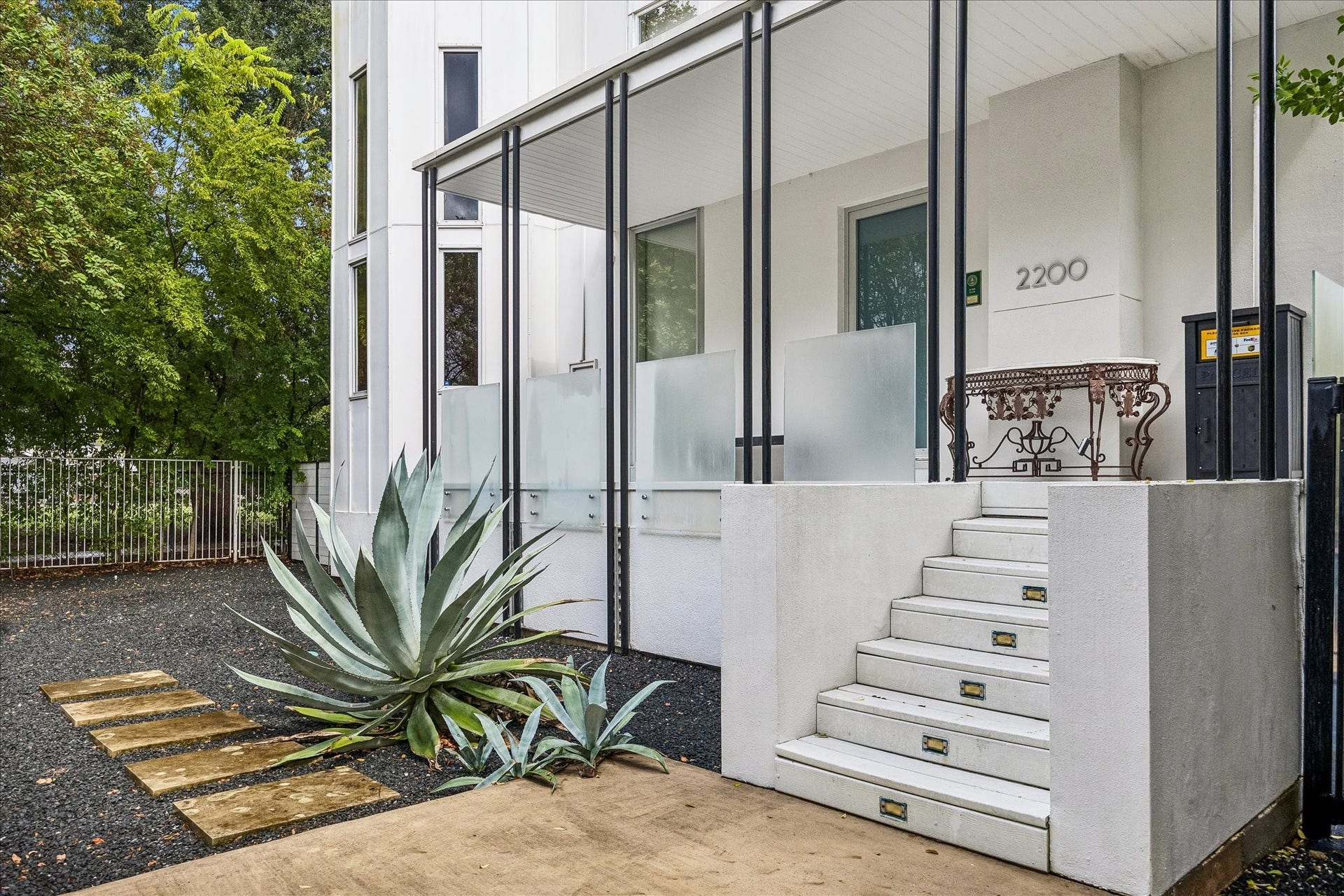 2200 Harvard Street, Houston, TX 77008 A sculptural agave and stepping-stone path lead to the elevated entry, where slender black columns and frosted glass panels reinforce the homes modern architectural character.