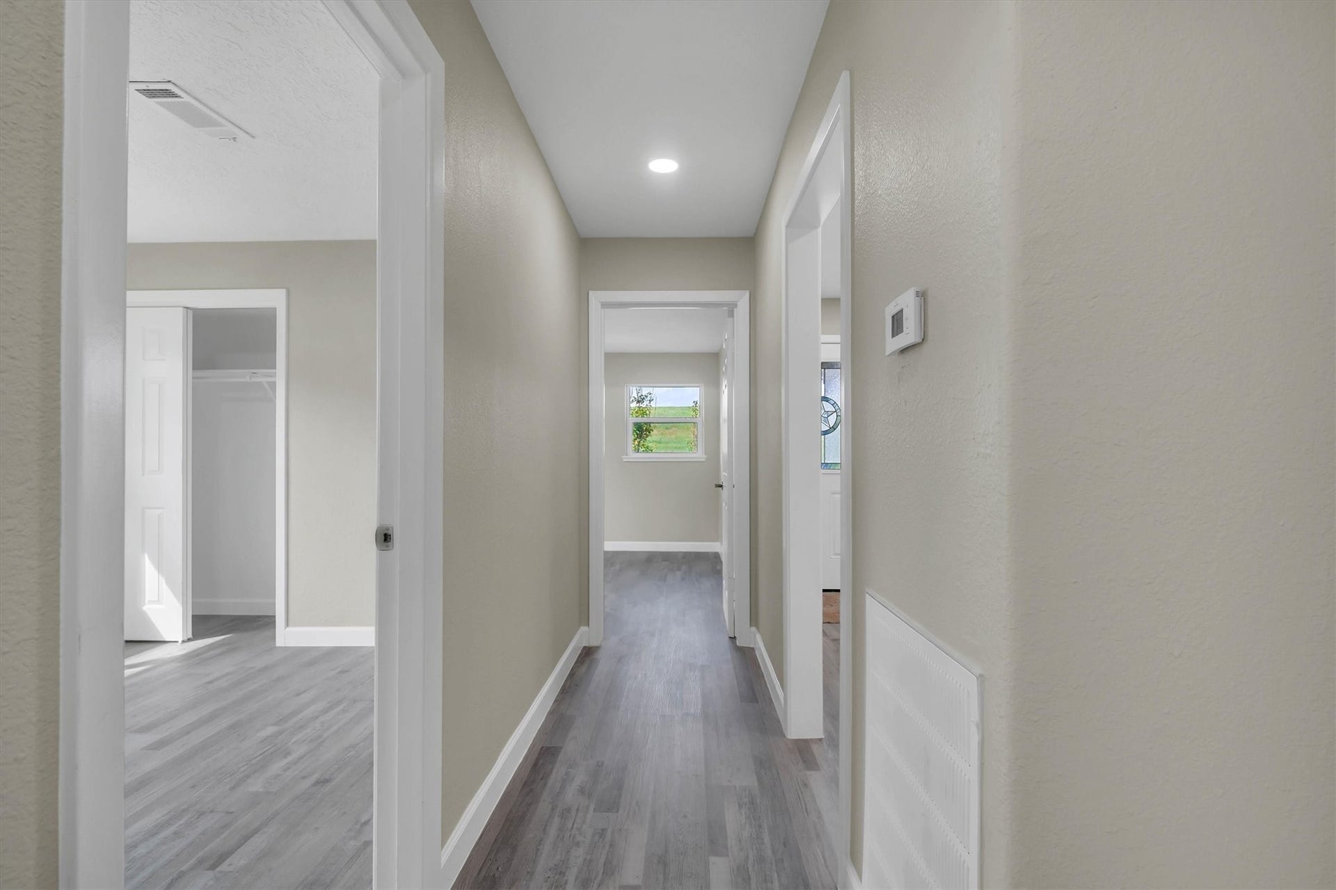 A bright, inviting hallway with modern flooring leads to multiple rooms, featuring fresh, neutral paint and recessed lighting for a clean, contemporary feel.