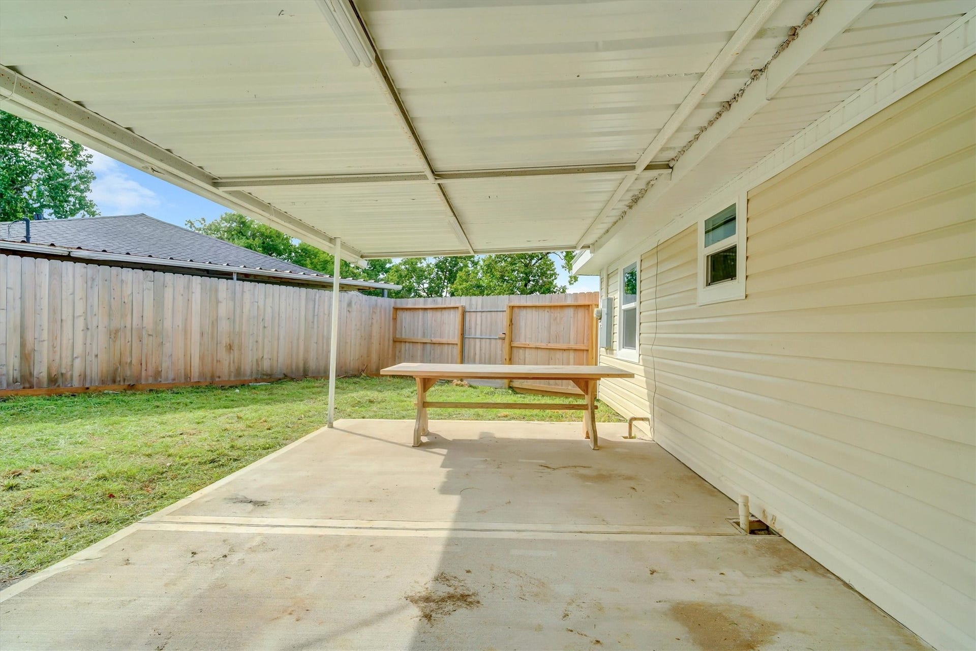 Covered patio with ample space for outdoor dining, overlooking a fenced backyard for added privacy.