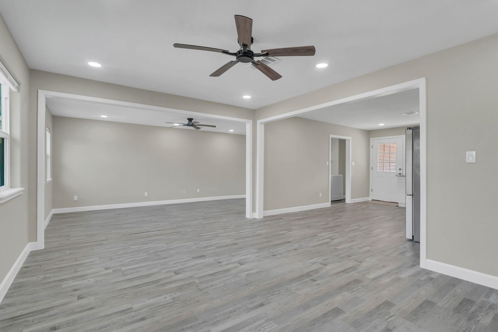 Spacious open-concept living area with stylish laminate flooring, modern ceiling fans, and ample natural light, leading to a bright kitchen space.