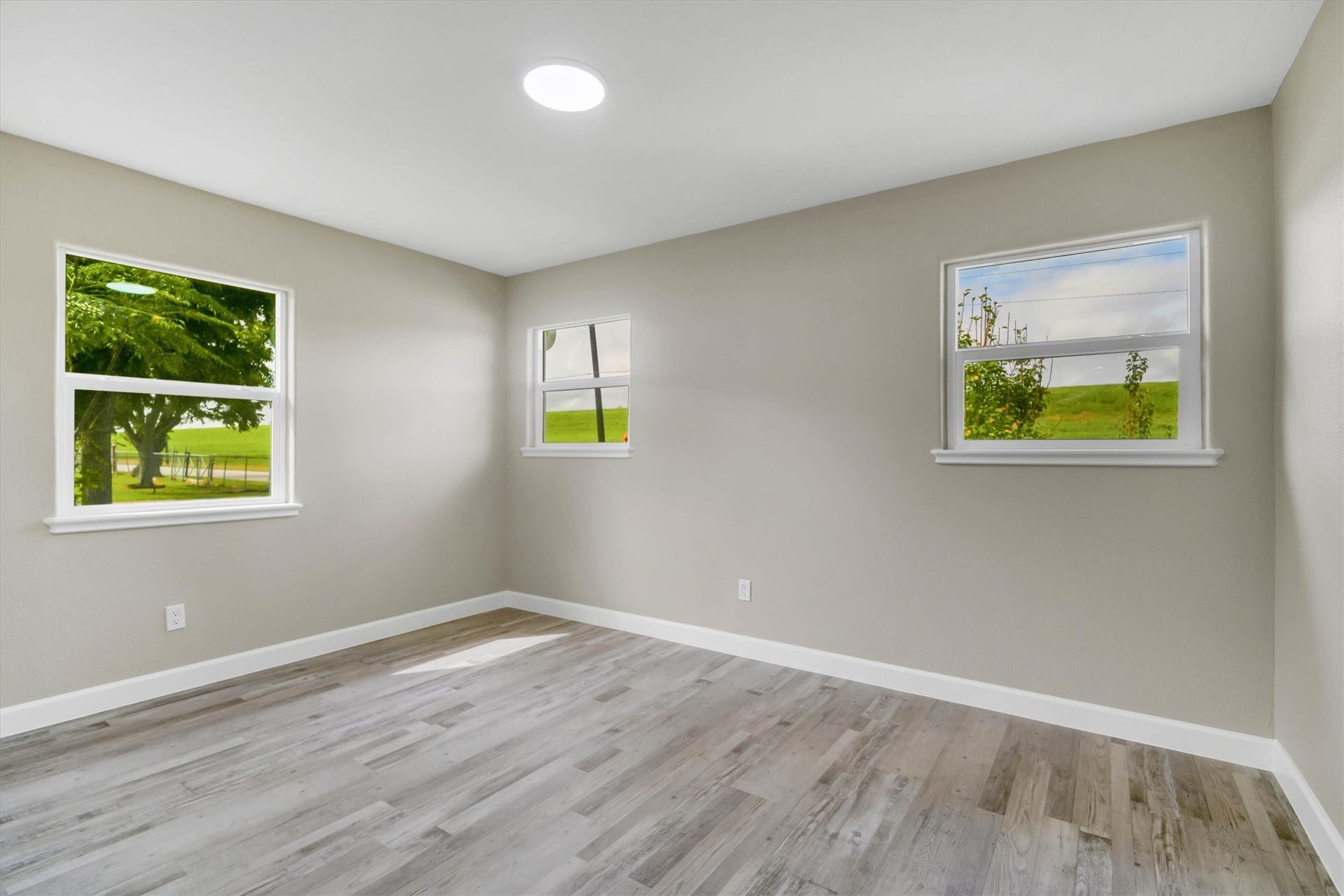 Bright and airy secondary bedroom with large windows offering plenty of natural light, complemented by neutral walls.