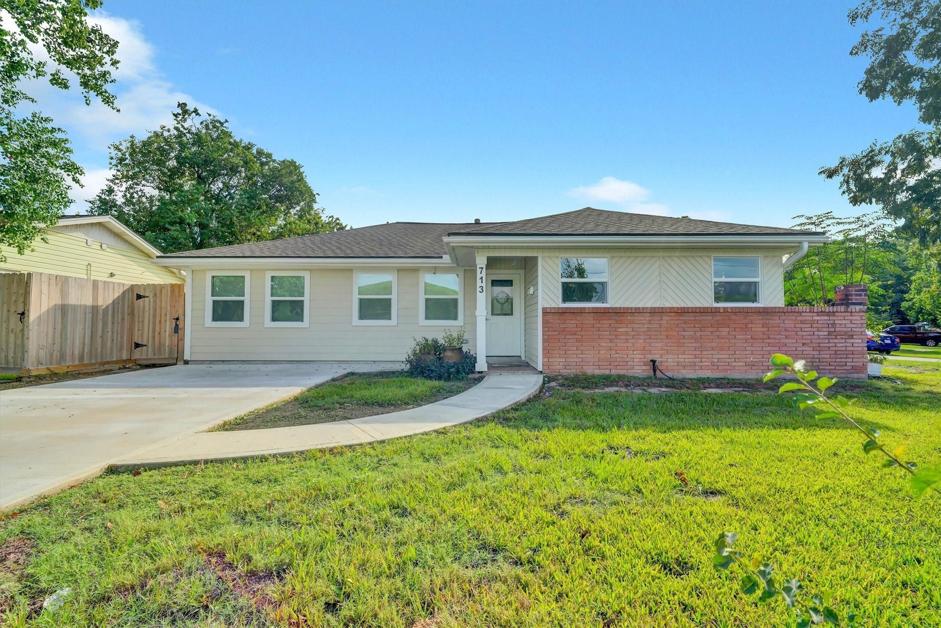 Charming single-story home with a welcoming brick facade, spacious front lawn, and a private driveway leading to a gated side entrance.
