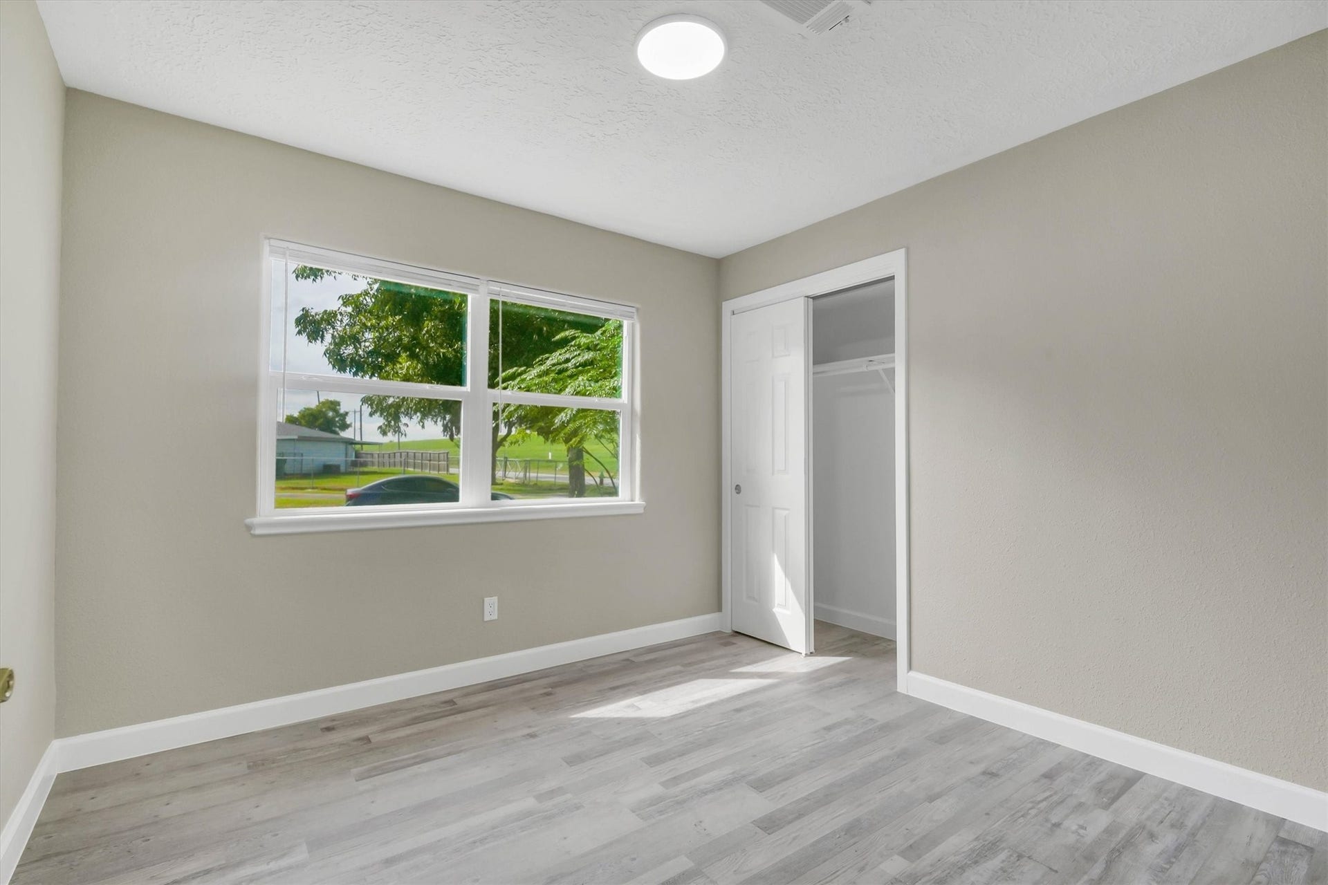 Bright room with large window, fresh neutral walls, and sleek gray flooring, featuring a cozy closet with sliding door.