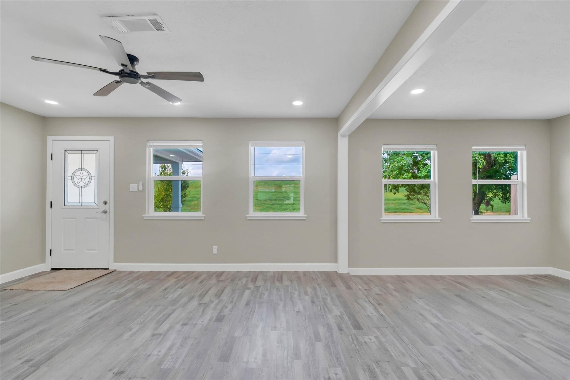Spacious living area with elegant laminate flooring, abundant natural light from multiple windows, and a stylish ceiling fan for added comfort.
