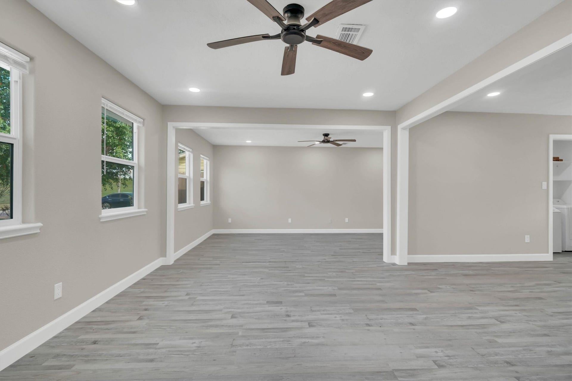 Living area with modern gray flooring, neutral walls, and ceiling fans, offering a bright and versatile space for any decor style.