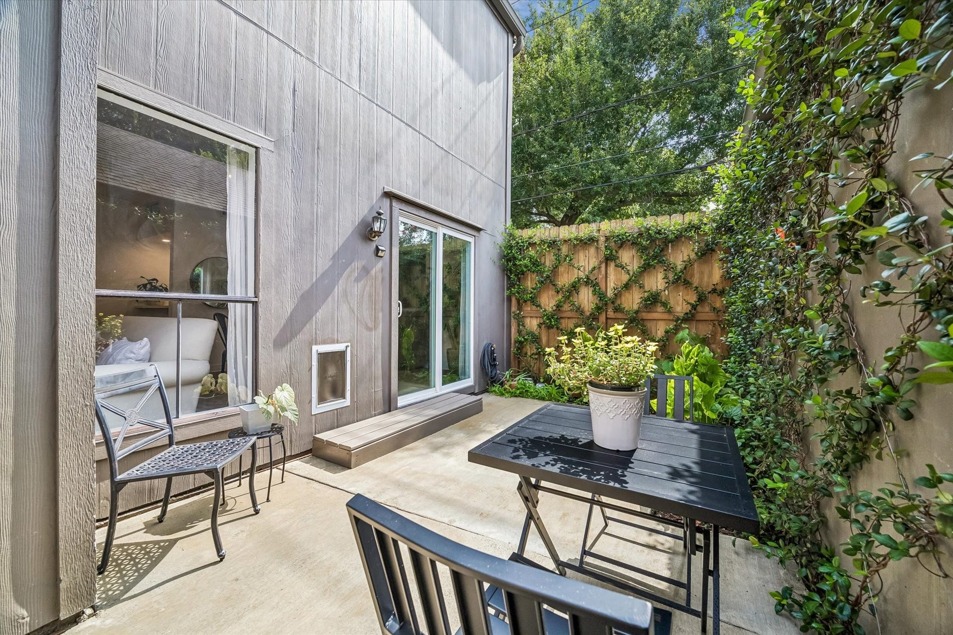 Charming private patio with a cozy seating area, lush greenery, and direct access to the home through sliding glass doors.