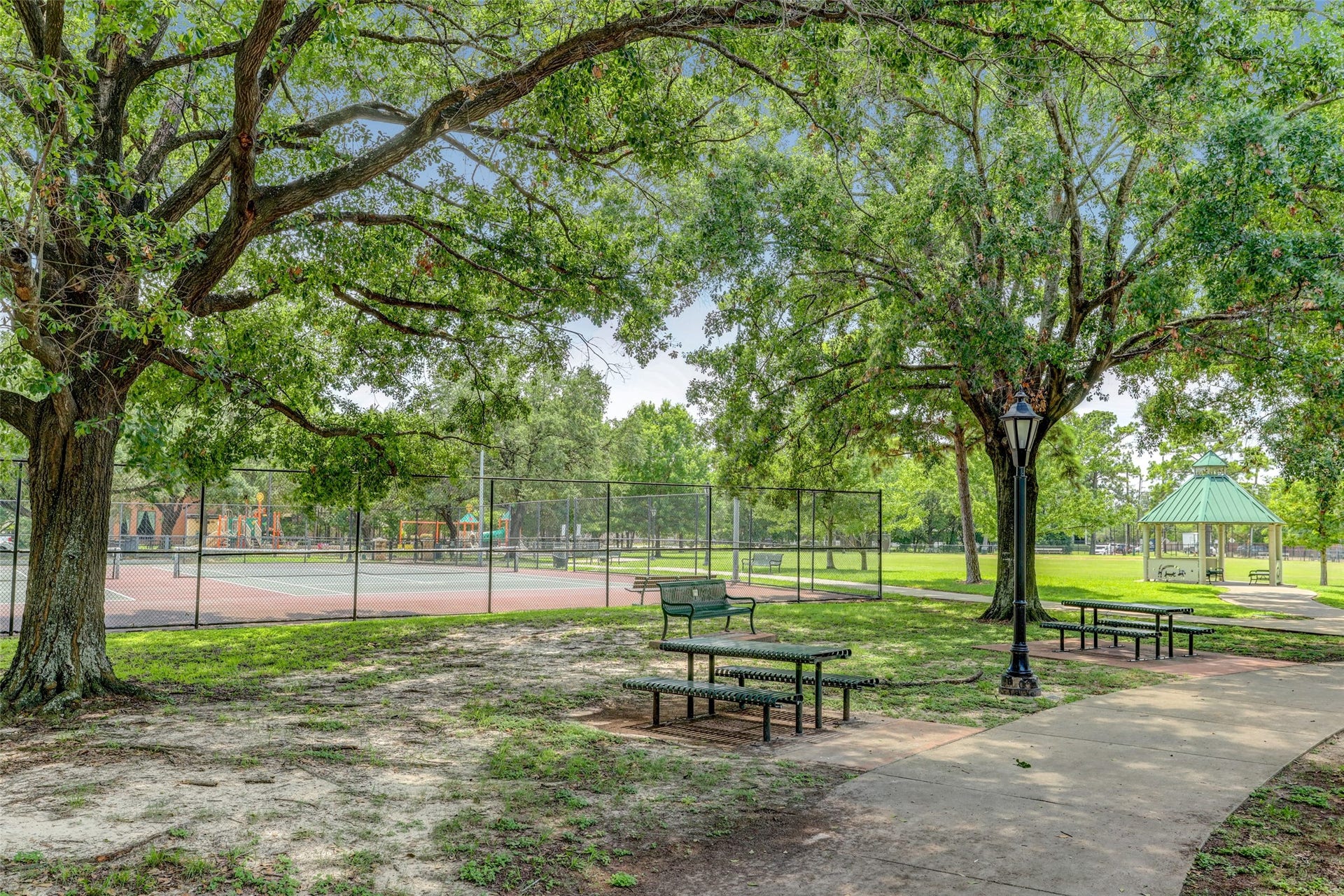 A serene park setting featuring lush trees, a playground, tennis courts, and a charming gazebo, perfect for outdoor relaxation and recreation.