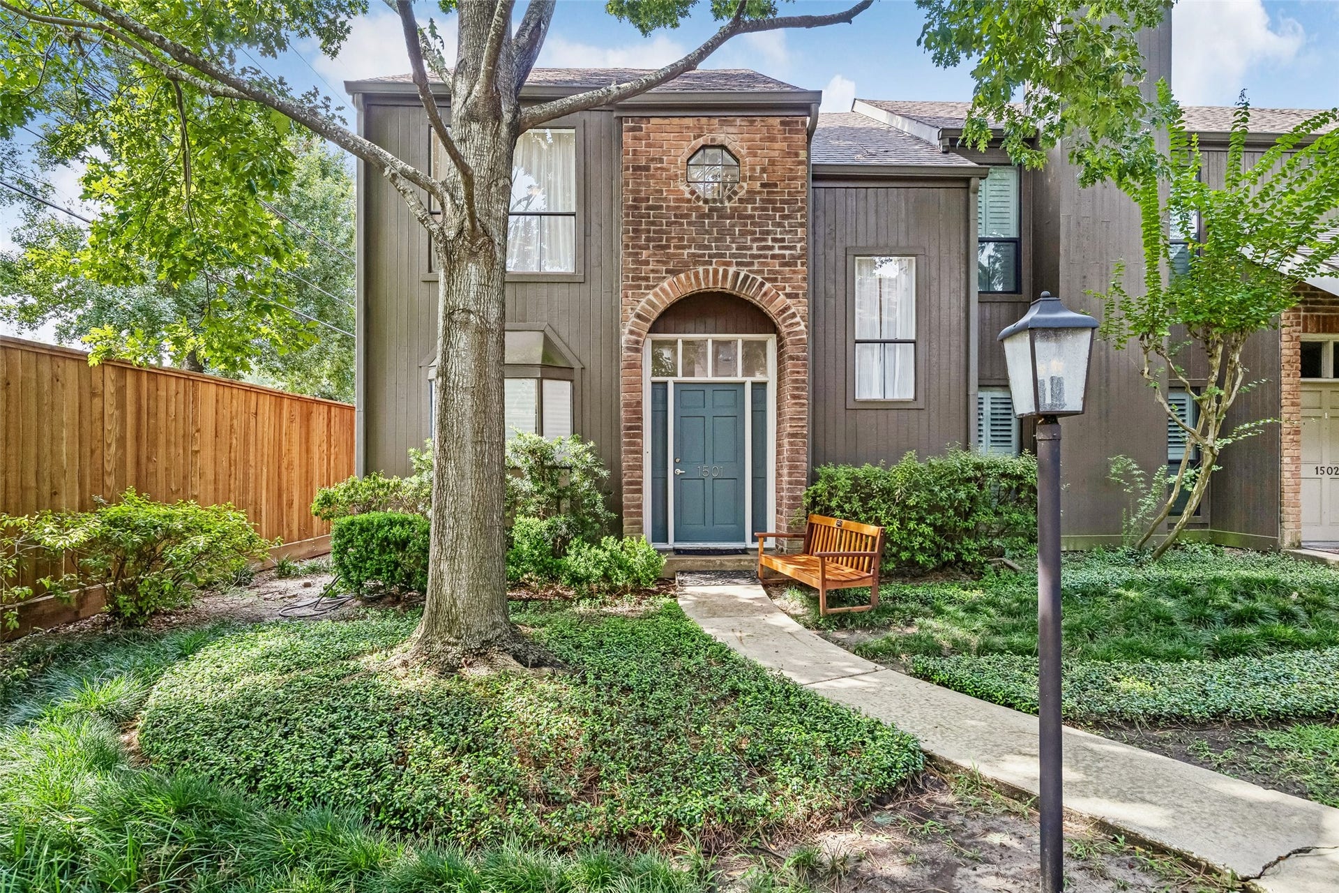 Charming townhouse featuring a welcoming brick archway, lush landscaping, creating a serene and inviting atmosphere.