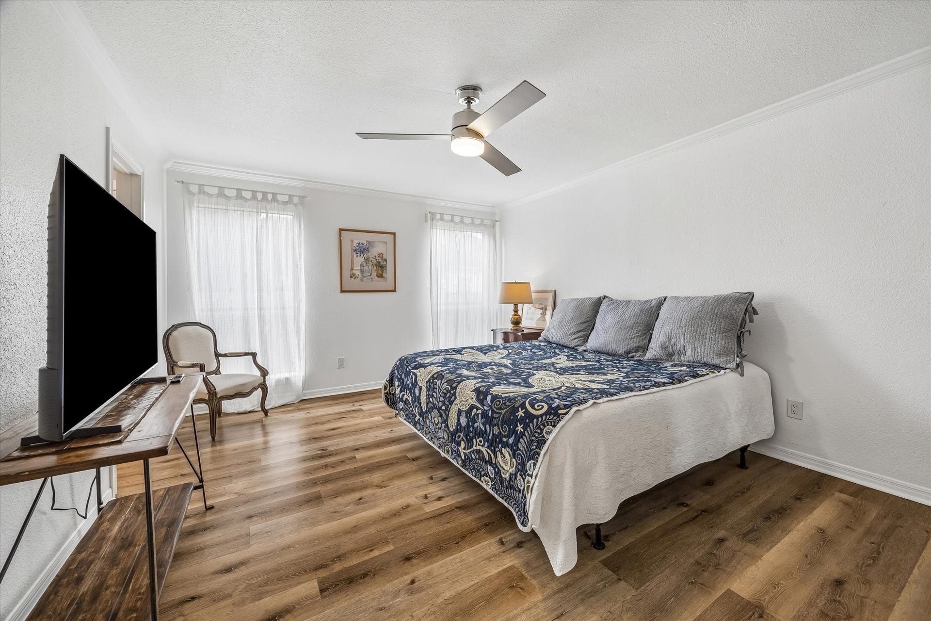 Primary bedroom featuring new vinyl plank flooring, a stylish ceiling fan, and ample natural light from large windows, creating a serene retreat.