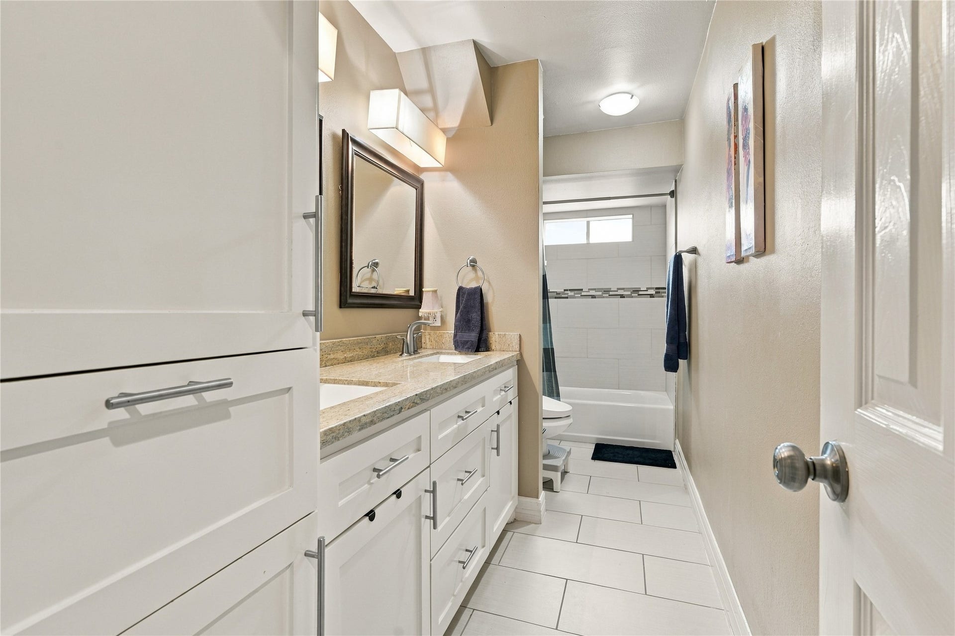 3211 Chris Drive, Houston, TX 77063 This secondary full bath features a white shaker vanity, a granite countertop & tall linen cabinet. The tub/shower combination is finished in white tile with a mosaic accent band.