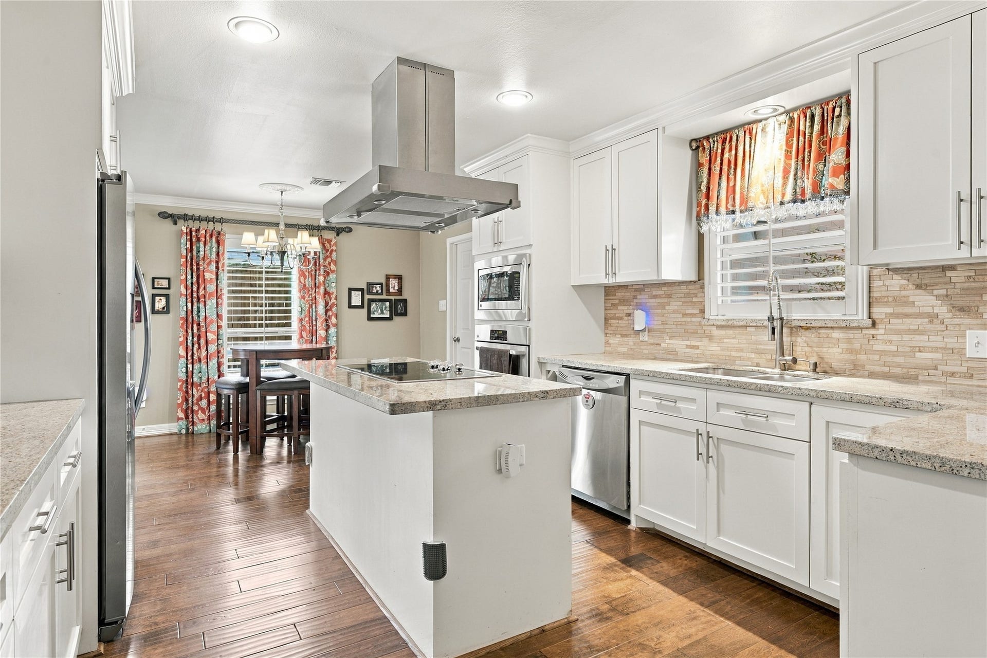 3211 Chris Drive, Houston, TX 77063 This bright kitchen features white shaker cabinetry, granite countertops, a linear stone mosaic backsplash & stainless steel appliances. The center island houses a smooth-top cooktop beneath a stainless chimney hood, and the wood floors flow into the breakfast room.