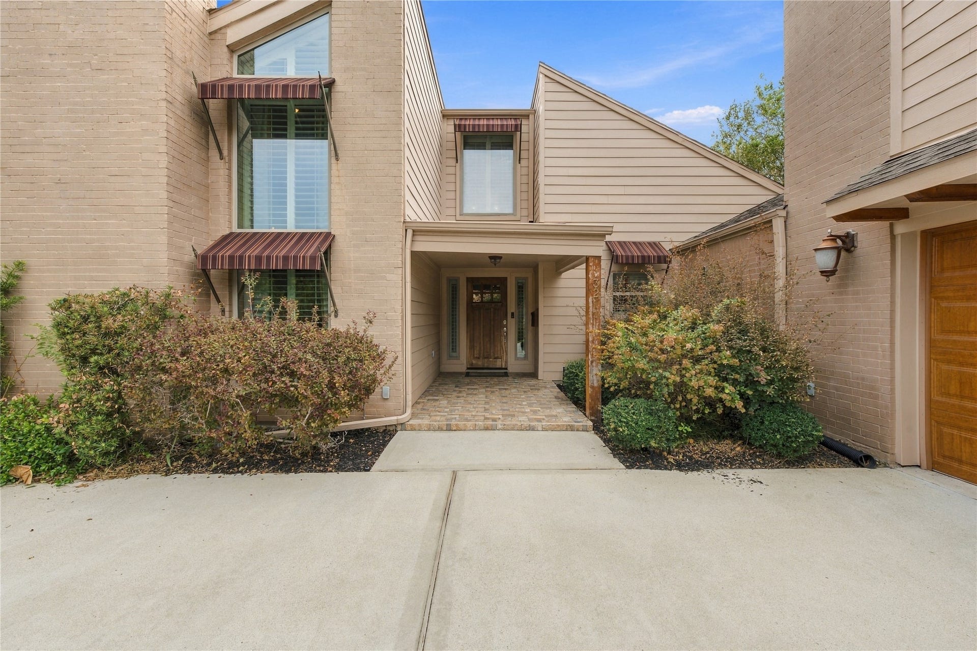 3211 Chris Drive, Houston, TX 77063 Covered entry features a brick-paver landing, solid wood front door w/ glass sidelights & tall windows topped by striped awnings on either side.