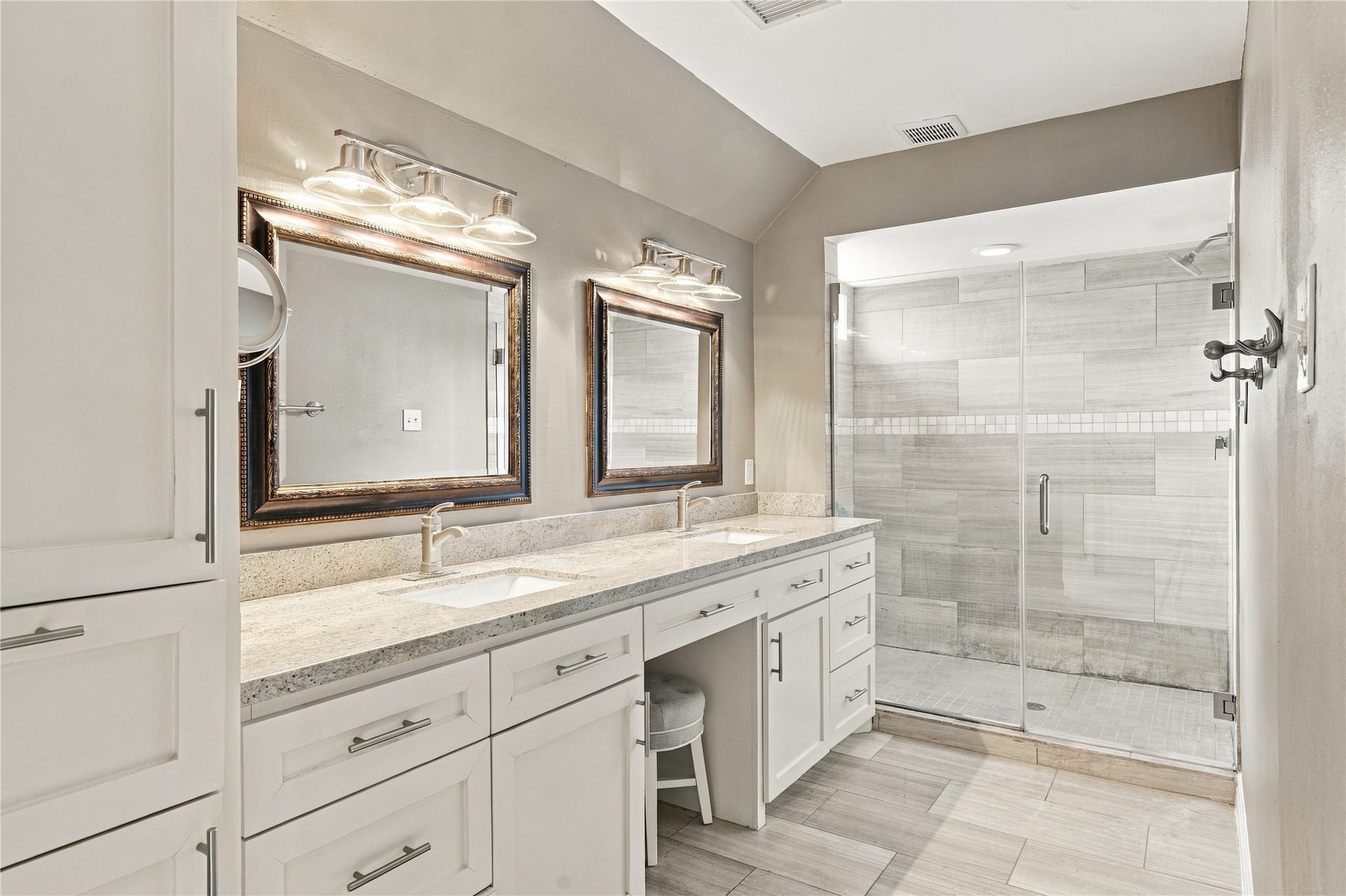 3211 Chris Drive, Houston, TX 77063 Spa-inspired primary bath features a white shaker dual vanity with granite countertop & built-in makeup station. The oversized frameless glass walk-in shower is wrapped floor to ceiling in large-format gray plank tile with a mosaic accent band.