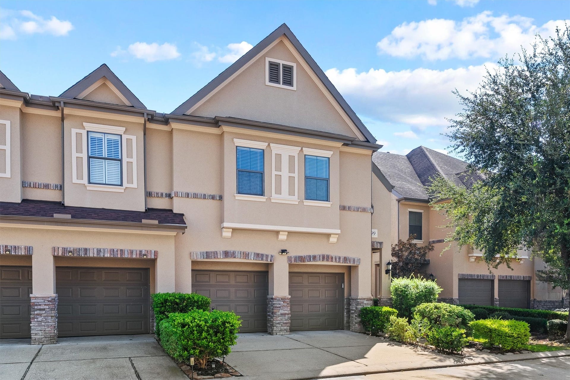 2919 Royal Oaks Crest, Houston, TX 77082 A townhouse with elegant composition roofs and stone-accented exteriors, featuring a spacious two-car garage and lush landscaping.