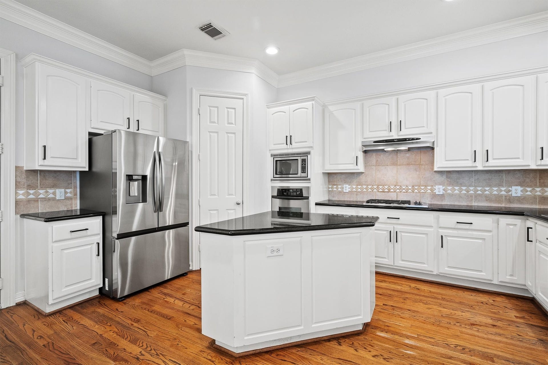 2919 Royal Oaks Crest, Houston, TX 77082 Bright and spacious kitchen with sleek stainless steel appliances, elegant black countertops, and ample white cabinetry, complemented by warm hardwood floors.