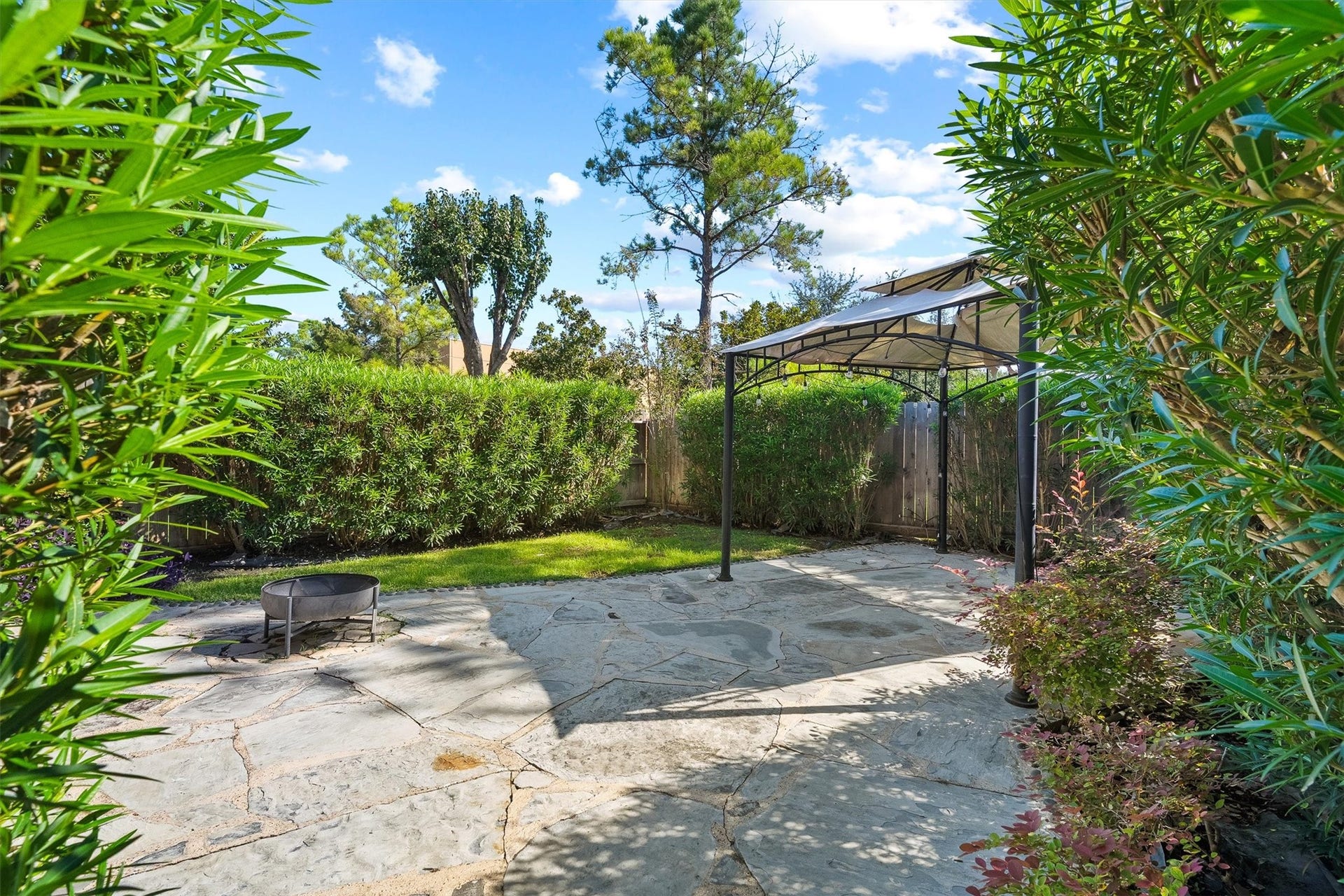 2919 Royal Oaks Crest, Houston, TX 77082 Nice backyard oasis featuring a stone patio with a gazebo, surrounded by lush greenery and a cozy fire pit, perfect for outdoor relaxation and entertaining.