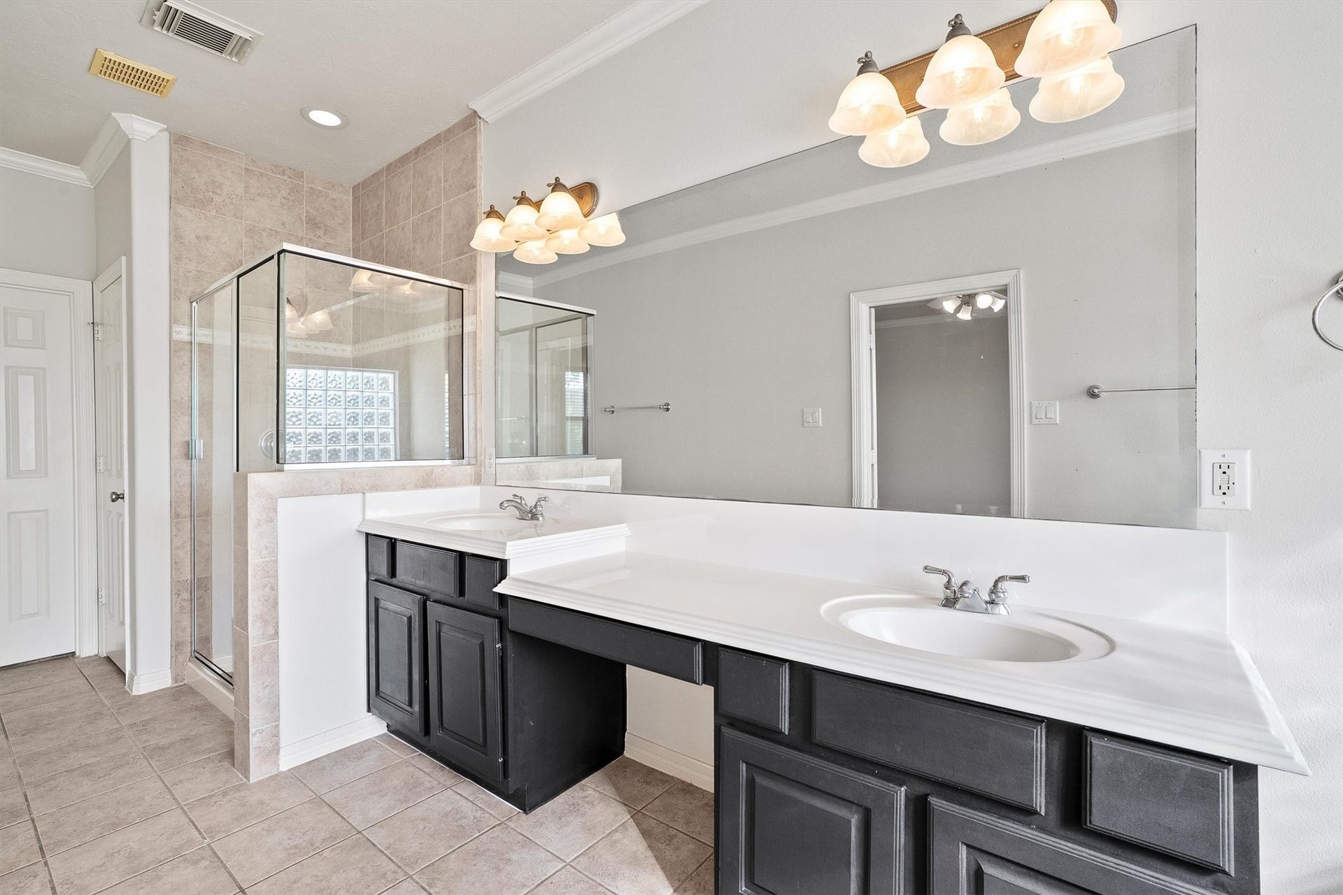 2919 Royal Oaks Crest, Houston, TX 77082 Spacious bathroom featuring a large glass-enclosed shower, dual sinks with elegant fixtures, and ample counter space with dark cabinetry, set against neutral tile flooring.