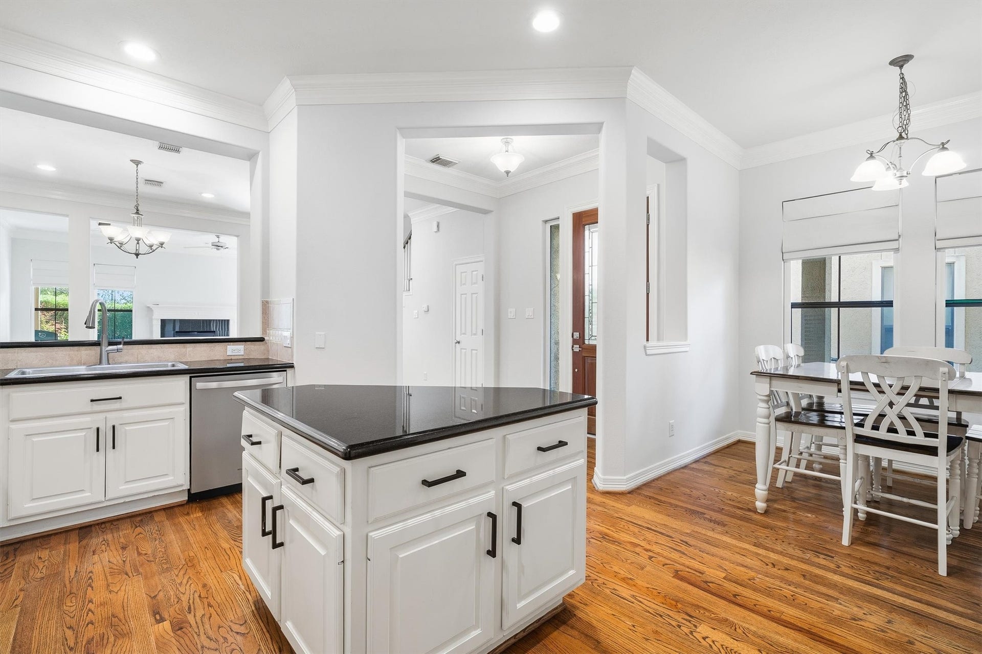 2919 Royal Oaks Crest, Houston, TX 77082 Bright and inviting kitchen features sleek black countertops, white cabinetry, and warm hardwood floors, seamlessly flowing into a cozy dining area with elegant lighting.