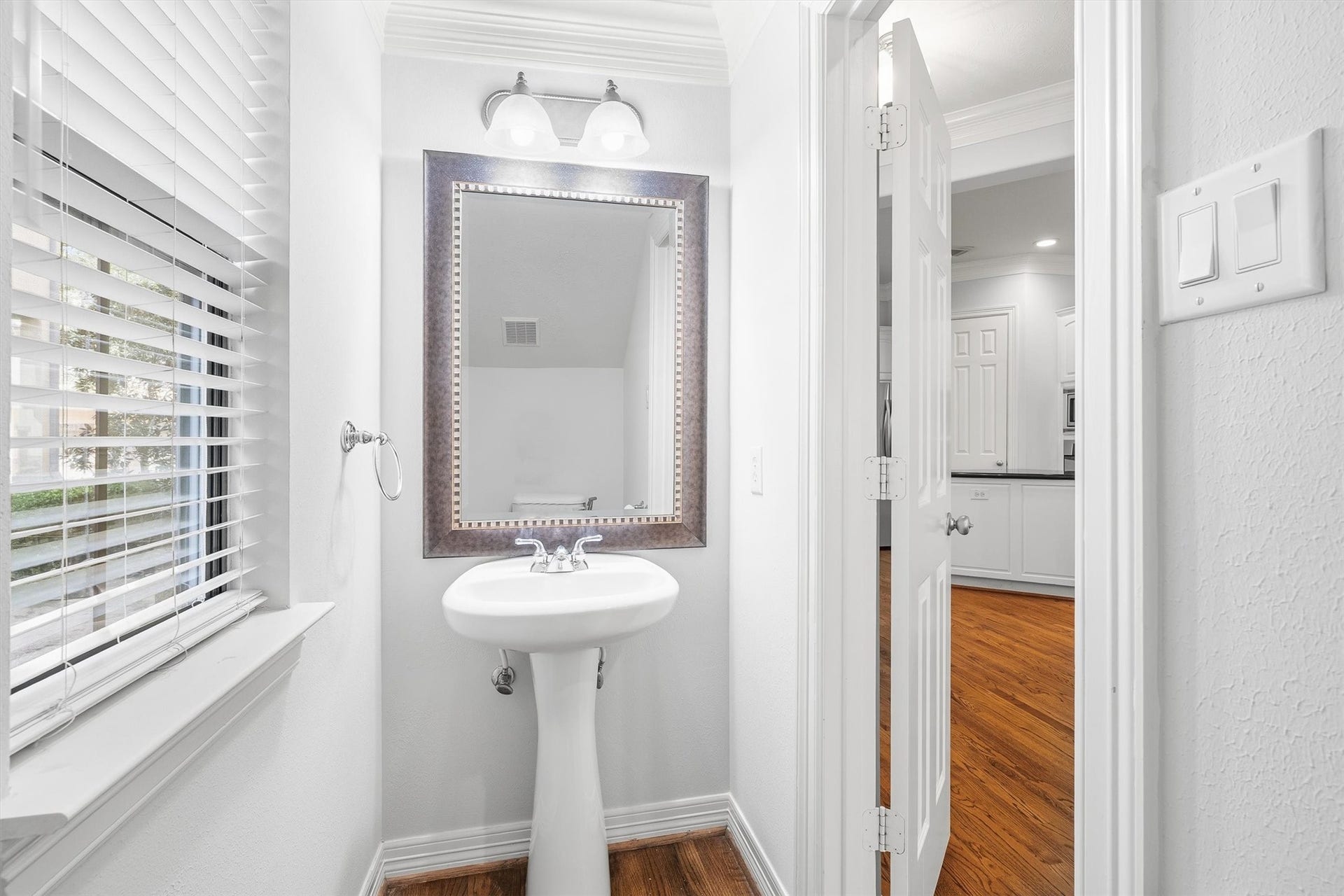 2919 Royal Oaks Crest, Houston, TX 77082 The powder room with a sleek pedestal sink, elegant mirror, and natural light streaming through a window with blinds.