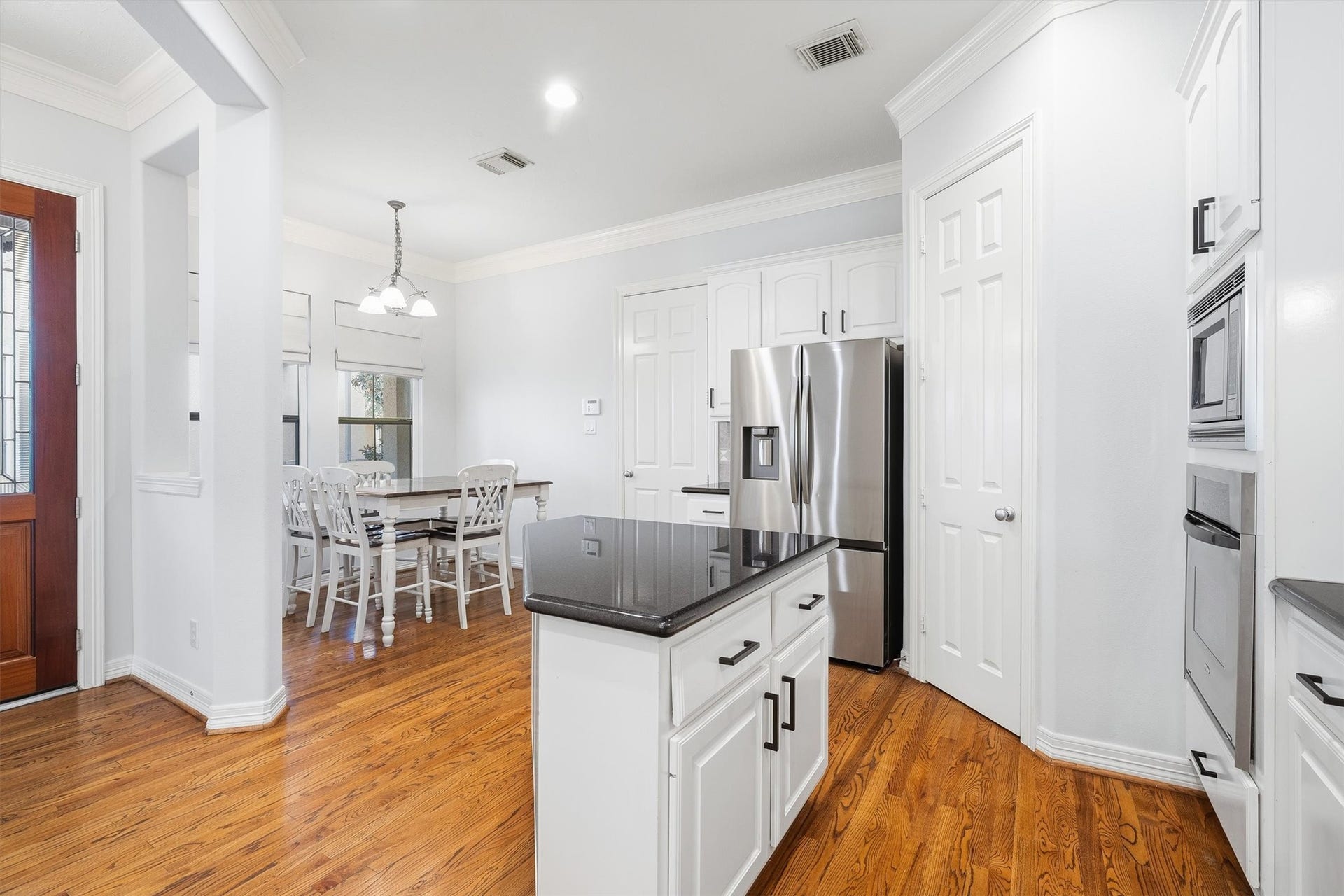 2919 Royal Oaks Crest, Houston, TX 77082 Bright kitchen with sleek black countertops, stainless steel appliances, and elegant wood flooring, seamlessly flowing into a cozy dining area with ample natural light.