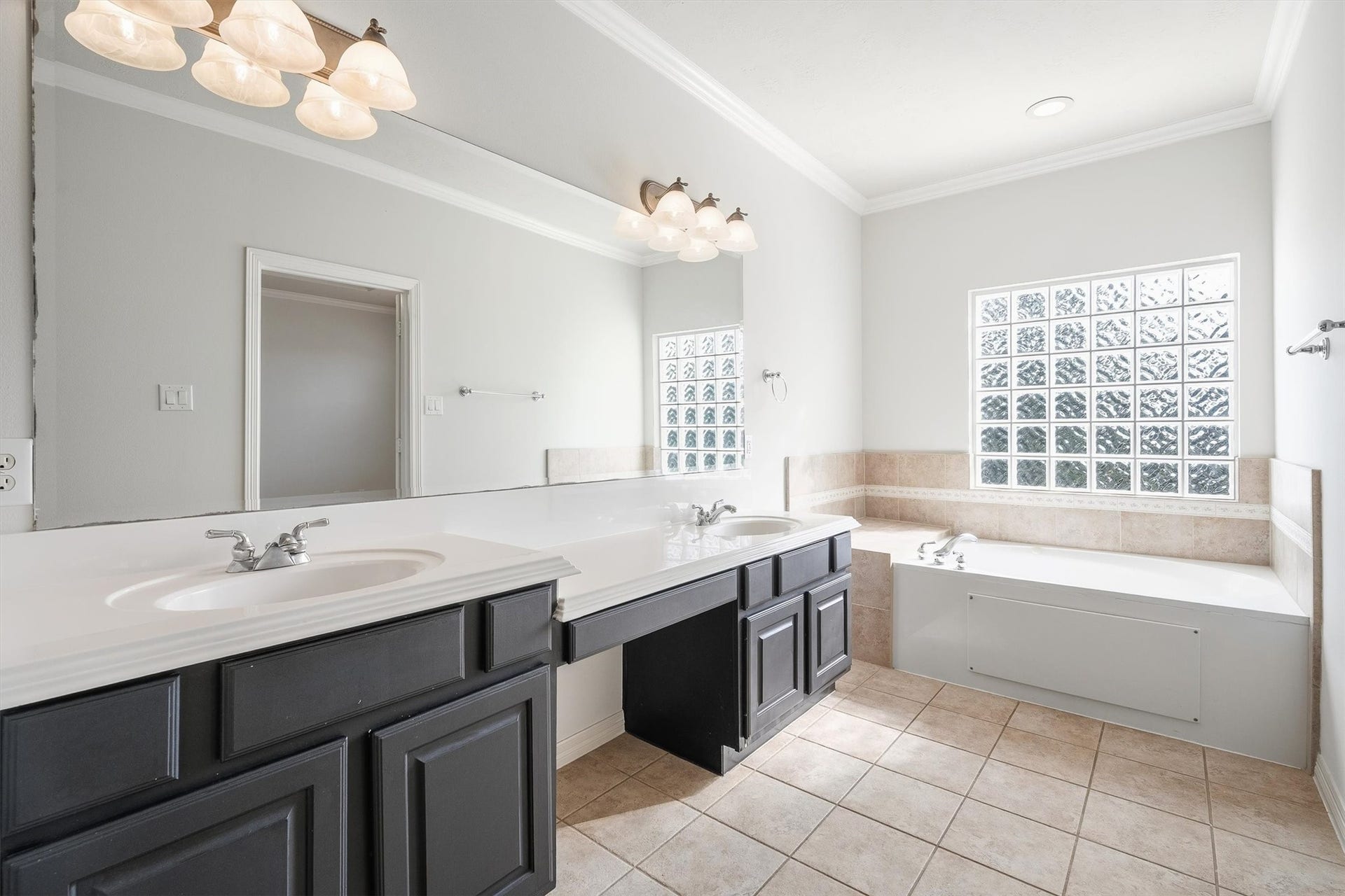 2919 Royal Oaks Crest, Houston, TX 77082 Bright and spacious bathroom featuring dual sinks, elegant fixtures, a large mirror, and a relaxing soaking tub, complemented by natural light from a stylish glass block window.