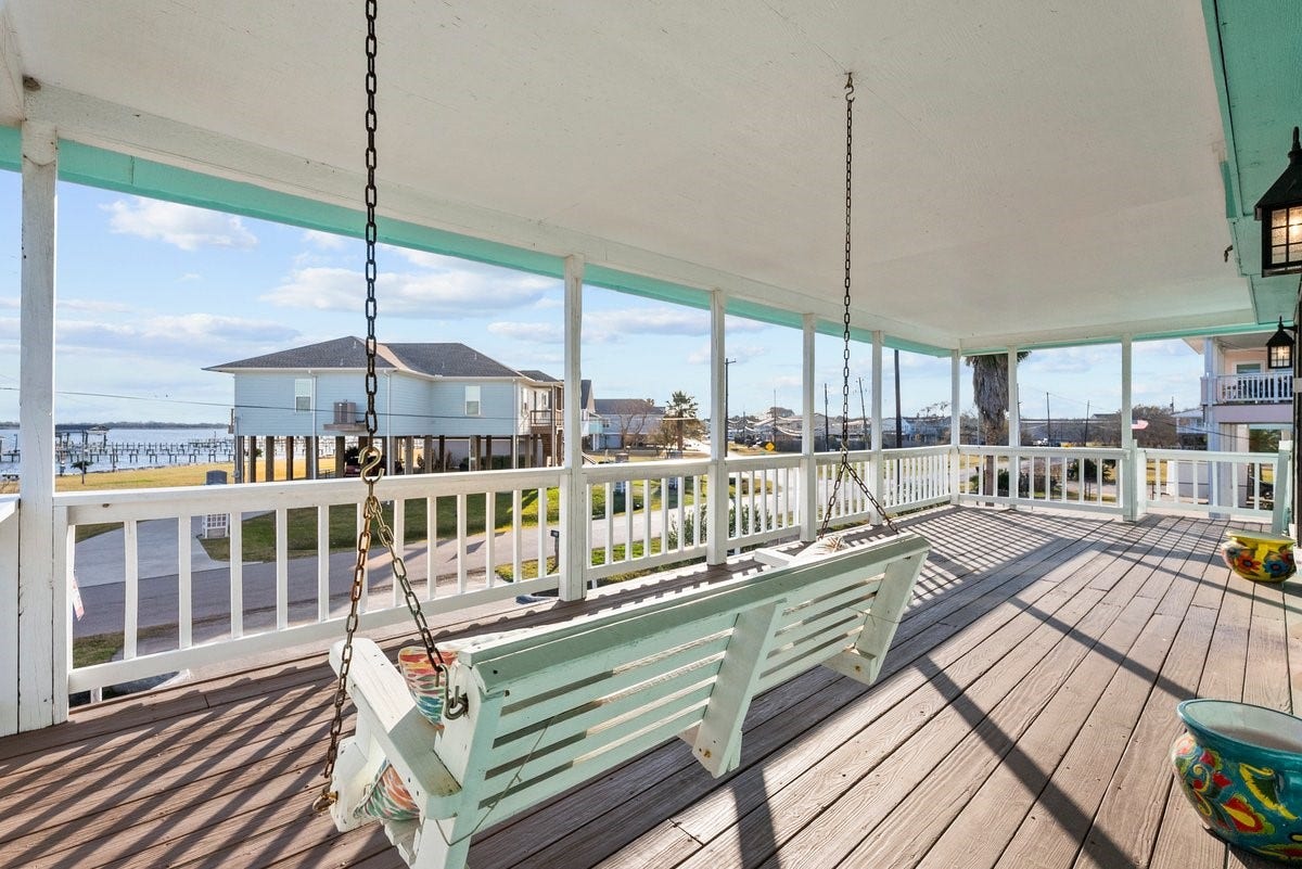 2406 Avenue P, San Leon, TX 77539 This spacious covered porch features a wooden swing and offers an inviting view of a coastal neighborhood, perfect for enjoying outdoor relaxation.