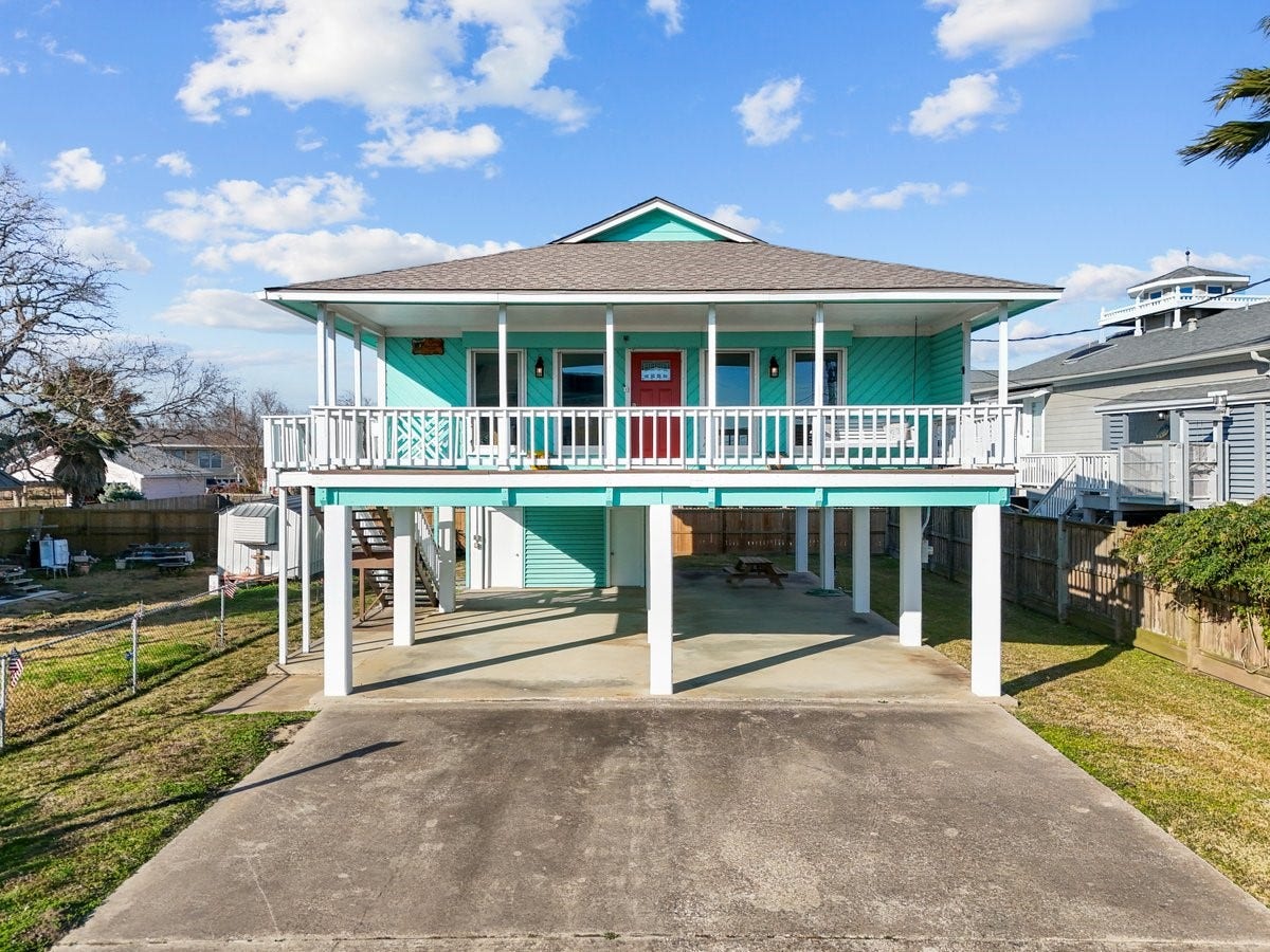 2406 Avenue P, San Leon, TX 77539 This elevated coastal home features a vibrant turquoise exterior, a spacious wraparound porch, and ample parking underneath. Ideal for enjoying seaside breezes and outdoor living.