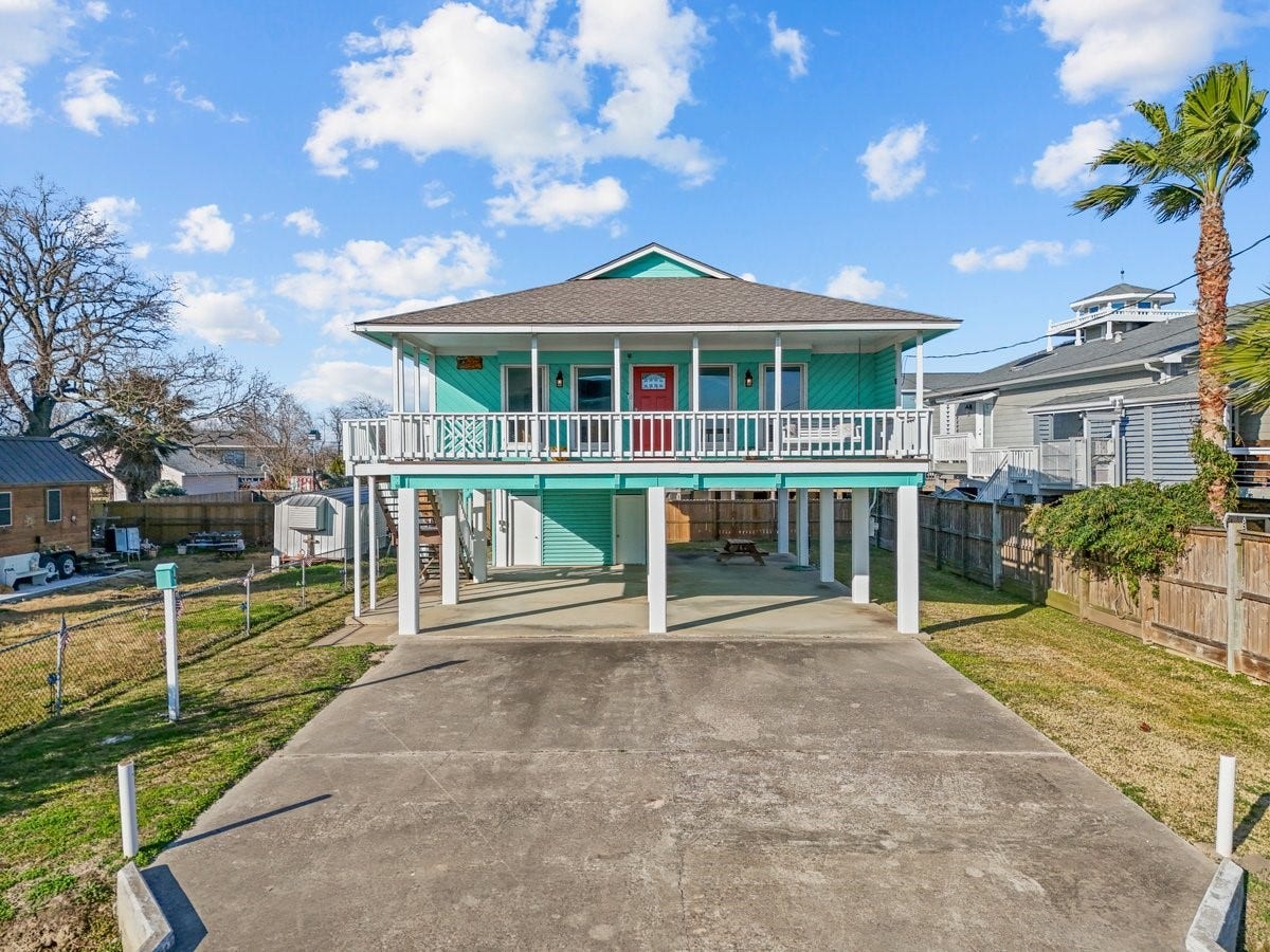 2406 Avenue P, San Leon, TX 77539 Elevated coastal home with a vibrant exterior, featuring a spacious driveway and covered parking. A wraparound porch provides charm and outdoor living space, while a fenced yard offers privacy. Perfect for enjoying seaside living.