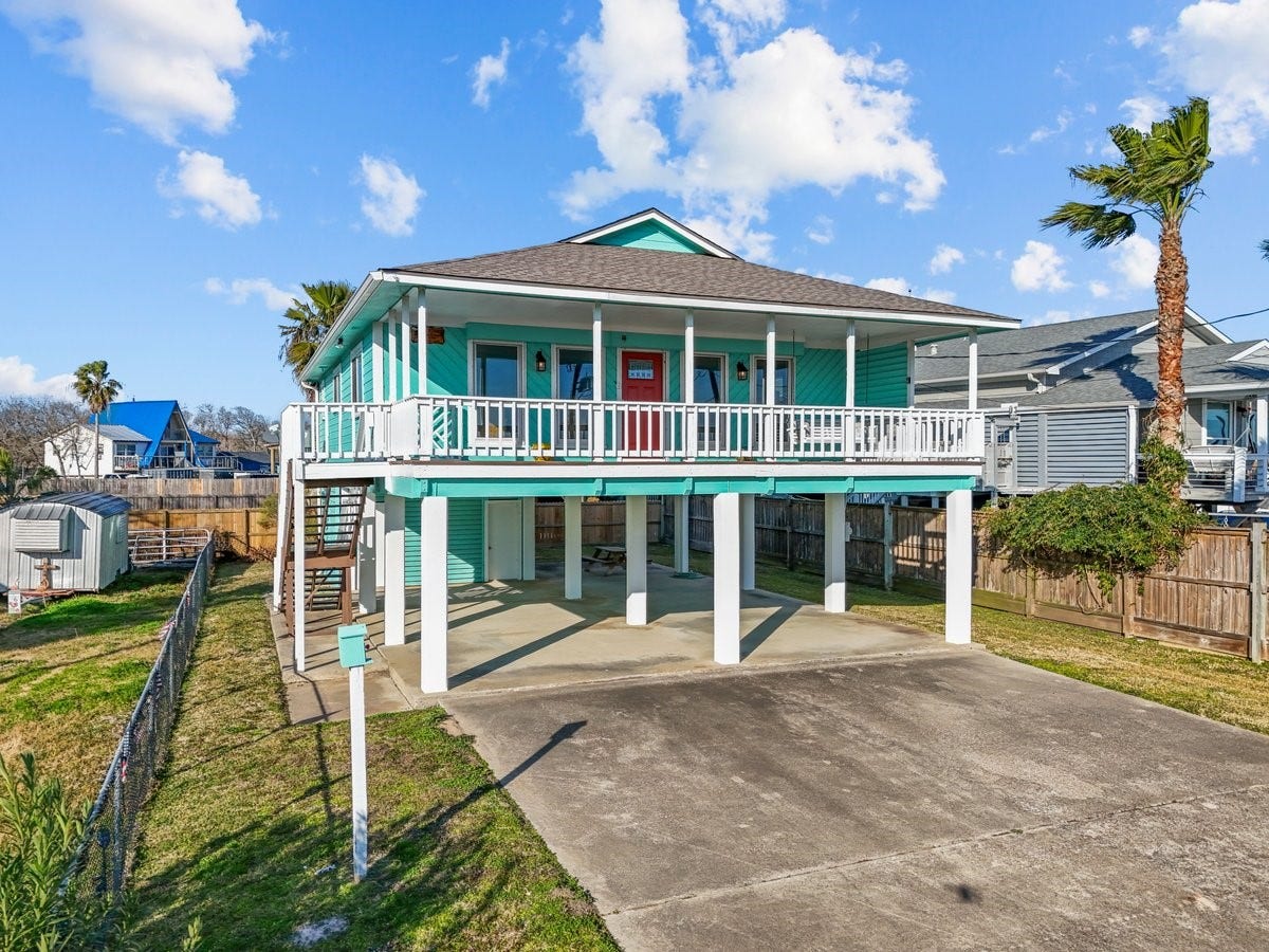 2406 Avenue P, San Leon, TX 77539 This elevated coastal home features a vibrant turquoise exterior with a spacious wraparound porch, covered parking, and a fenced yard. Ideal for enjoying beachside living.
