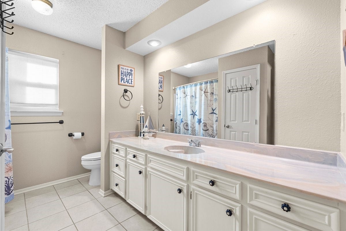 2406 Avenue P, San Leon, TX 77539 Bright and spacious bathroom with neutral tones, featuring a large mirror, ample counter space, and a decorative shower curtain. Ideal for comfort and style.