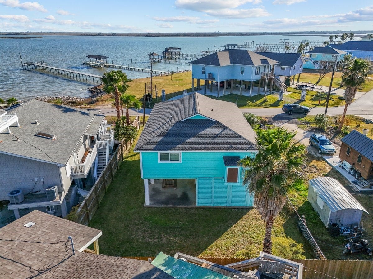 2406 Avenue P, San Leon, TX 77539 This photo showcases a charming waterfront home with a spacious yard, nestled near a serene body of water. The property includes a dock, offering direct access to the water, and is surrounded by other elevated homes, providing a picturesque coastal community vibe.