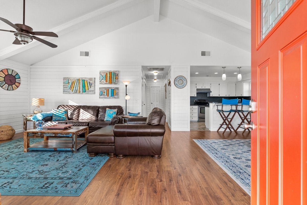 2406 Avenue P, San Leon, TX 77539 This open-concept living space features high vaulted ceilings and wood flooring, creating a spacious feel. The room is bright and welcoming with a pop of color from the orange door.