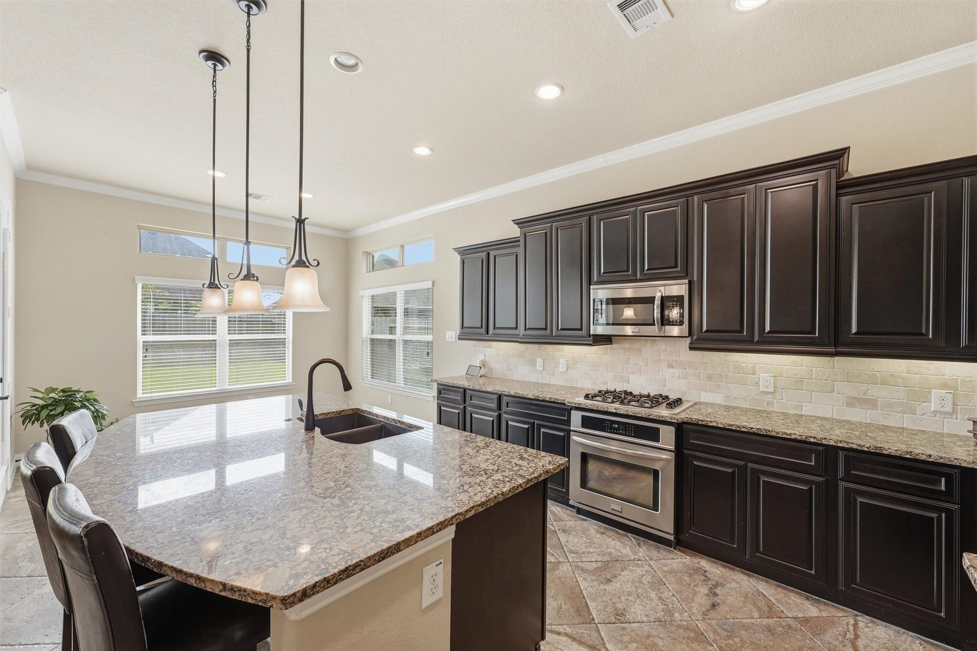Island kitchen with breakfast bar, granite counters, and stainless steel appliances - all overlooking the living room with views to the backyard retreat.