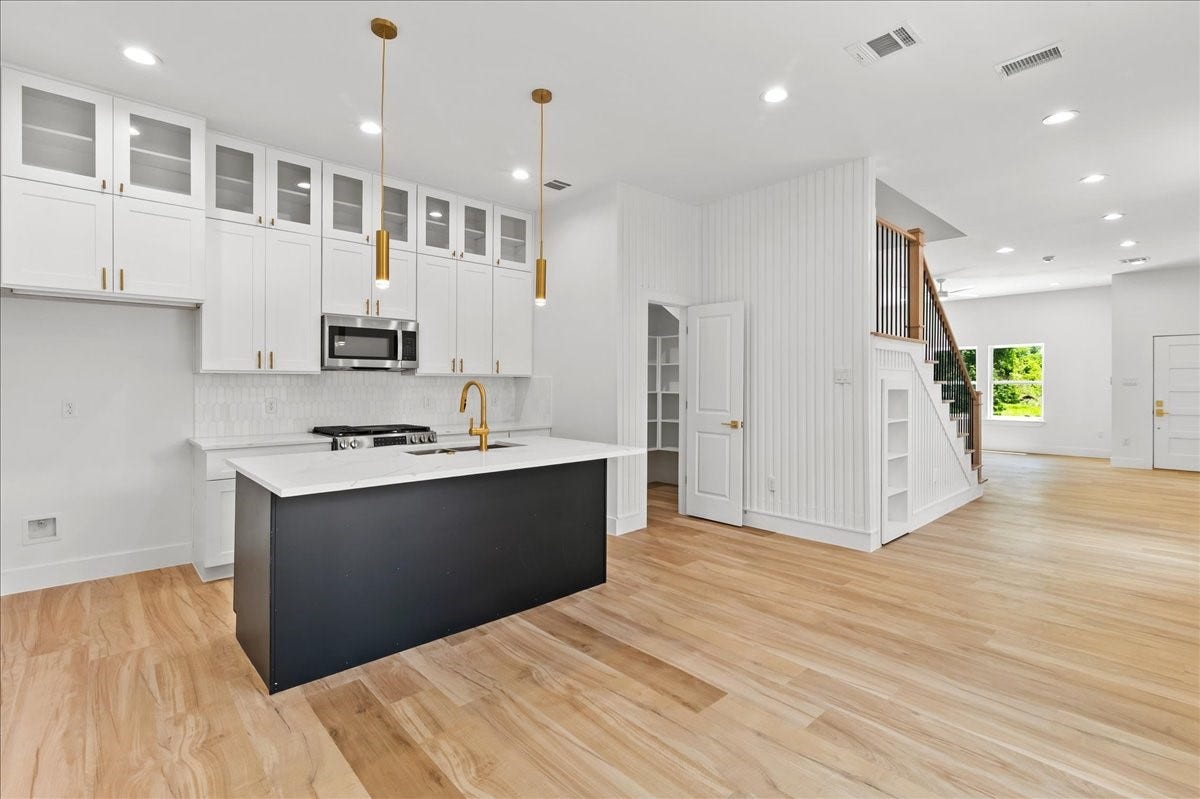 8323 Observatory Street, #A/B, Houston, TX 77088 Unit A - Designer kitchen featuring double-stacked white cabinetry, a striking black accent island, elegant gold fixtures, and stainless steel appliances, blending modern sophistication with everyday functionality. Accent Wall design may vary. Pictures are from a previous build.