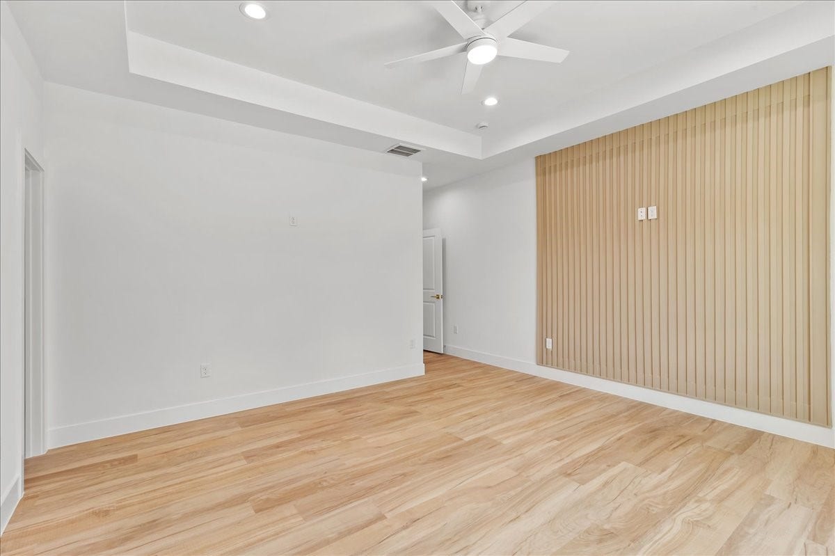 8323 Observatory Street, #A/B, Houston, TX 77088 Unit A - Spacious primary suite featuring a beautiful neutral-toned accent wall that perfectly complements the wood-look flooring, elegant coffered ceiling, and a remote-controlled ceiling fan.Accent Wall design may vary. Pictures are from a previous build.