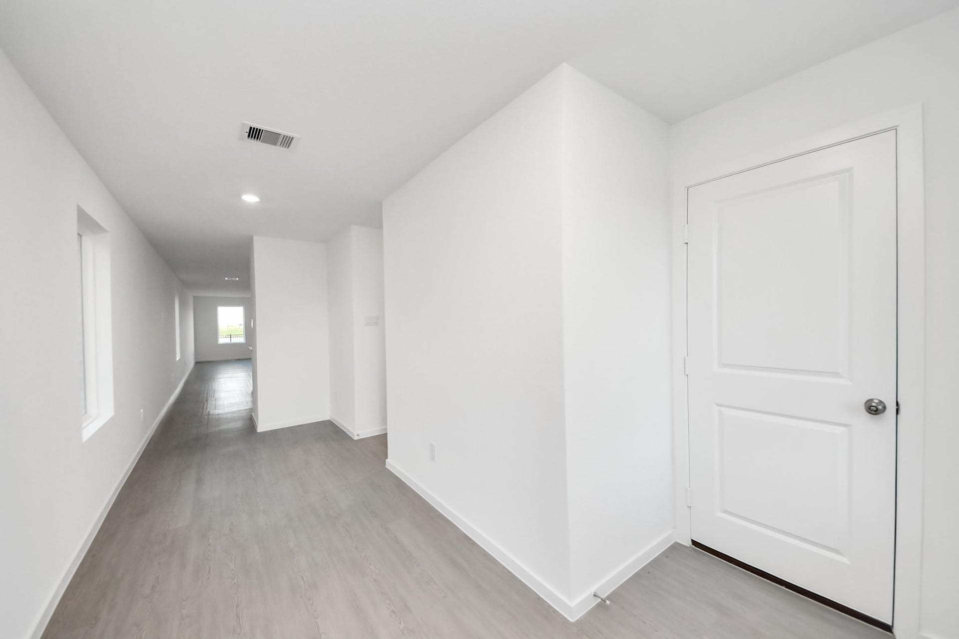 3096 Sunset Glory Drive, Katy, TX 77493 This photo shows a bright, minimalistic hallway with light wood flooring and white walls. It features recessed lighting and leads to a room with a window at the end, creating an airy, spacious feel.