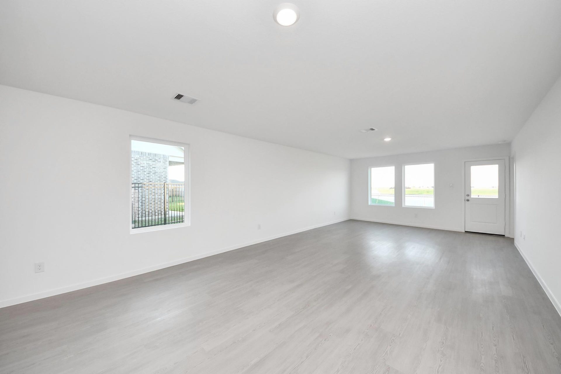 3096 Sunset Glory Drive, Katy, TX 77493 This spacious, bright room features light vinyl plank flooring, white walls, and ample natural light from two large windows and a door leading outside. Ideal for a living and dinning area.