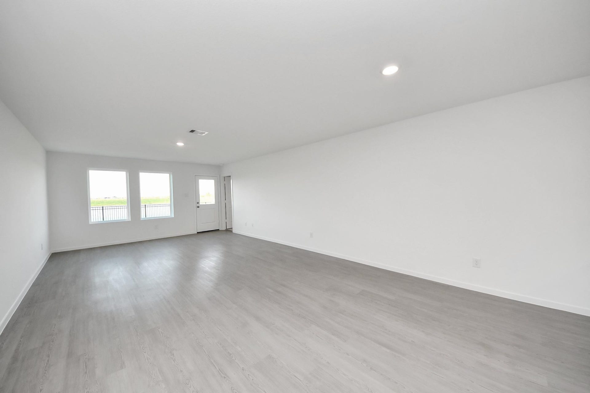 3096 Sunset Glory Drive, Katy, TX 77493 This spacious, bright living area and open concept dinning area features modern vinyl plank flooring, ample windows providing natural light, and a door leading outside. Perfect for versatile arrangements and comfortable living.