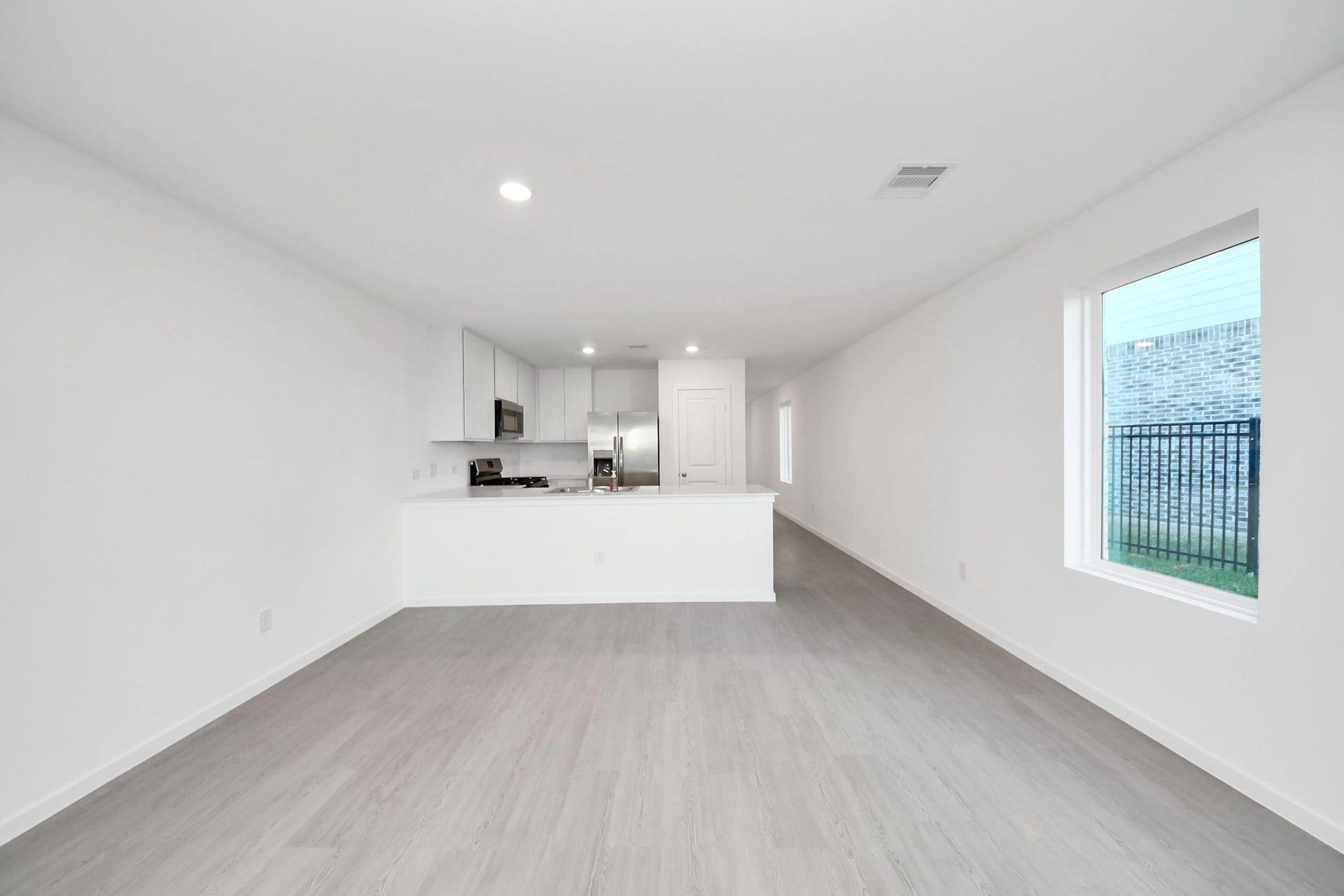 3096 Sunset Glory Drive, Katy, TX 77493 This photo showcases a modern, open-concept kitchen and living area with light wood flooring and white walls. The kitchen features sleek white cabinetry, stainless steel appliances, and a spacious countertop. Large windows let in natural light, adding to the bright and airy feel.