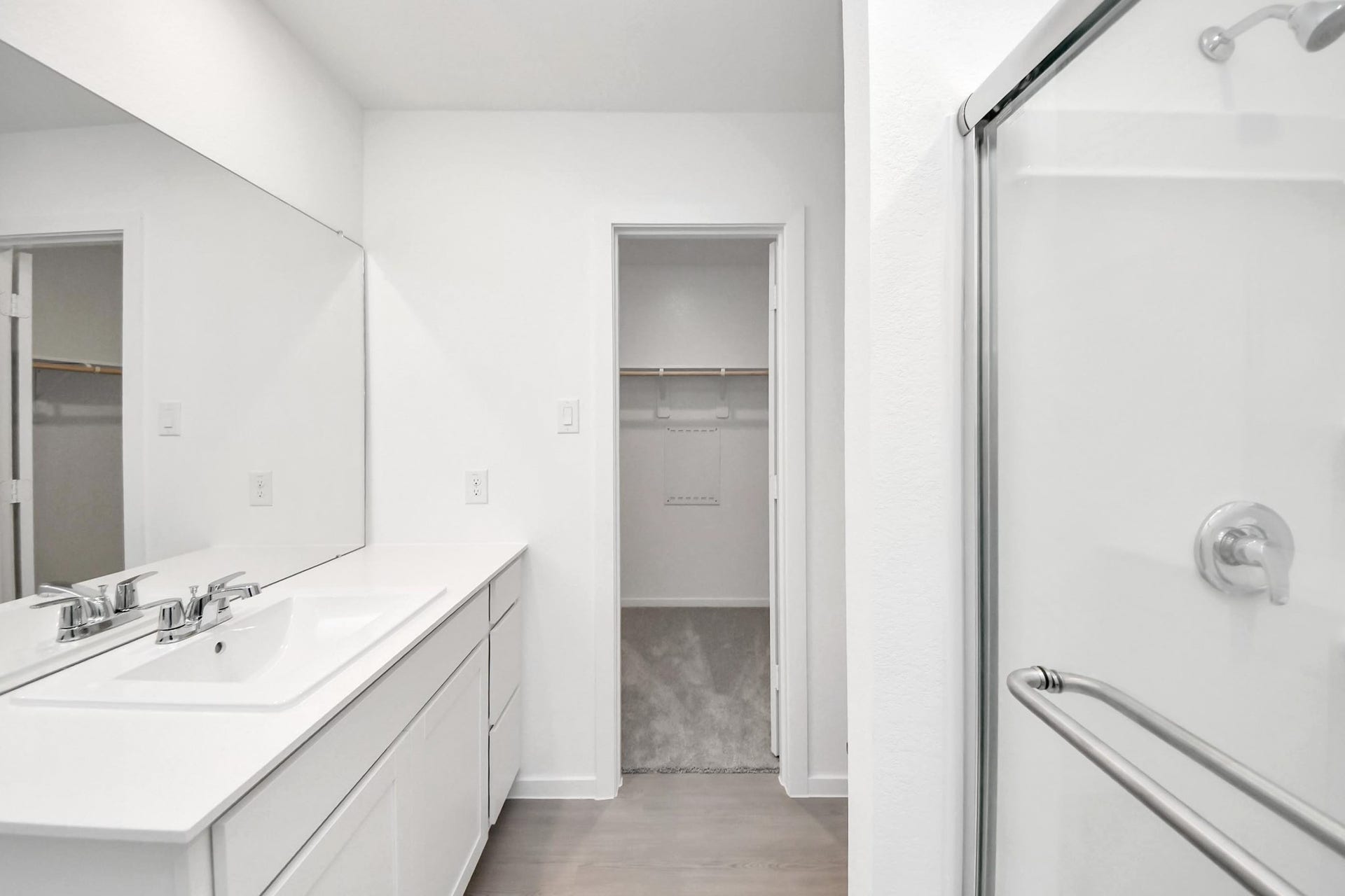 3096 Sunset Glory Drive, Katy, TX 77493 This photo showcases a modern bathroom featuring a sleek white quartz vanity with a large mirror, a glass-enclosed shower, and an adjacent walk-in closet for added convenience.