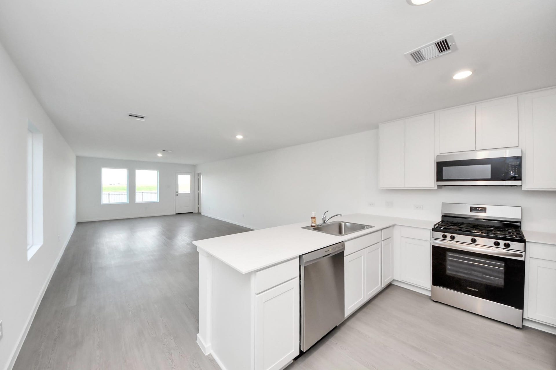 3096 Sunset Glory Drive, Katy, TX 77493 This photo showcases a modern, open-concept living area with light vinyl plank flooring and ample natural light. The kitchen features sleek white cabinetry, stainless steel appliances, and a spacious quartz island with a modern farmhouse sink, offering a seamless flow into the living space.