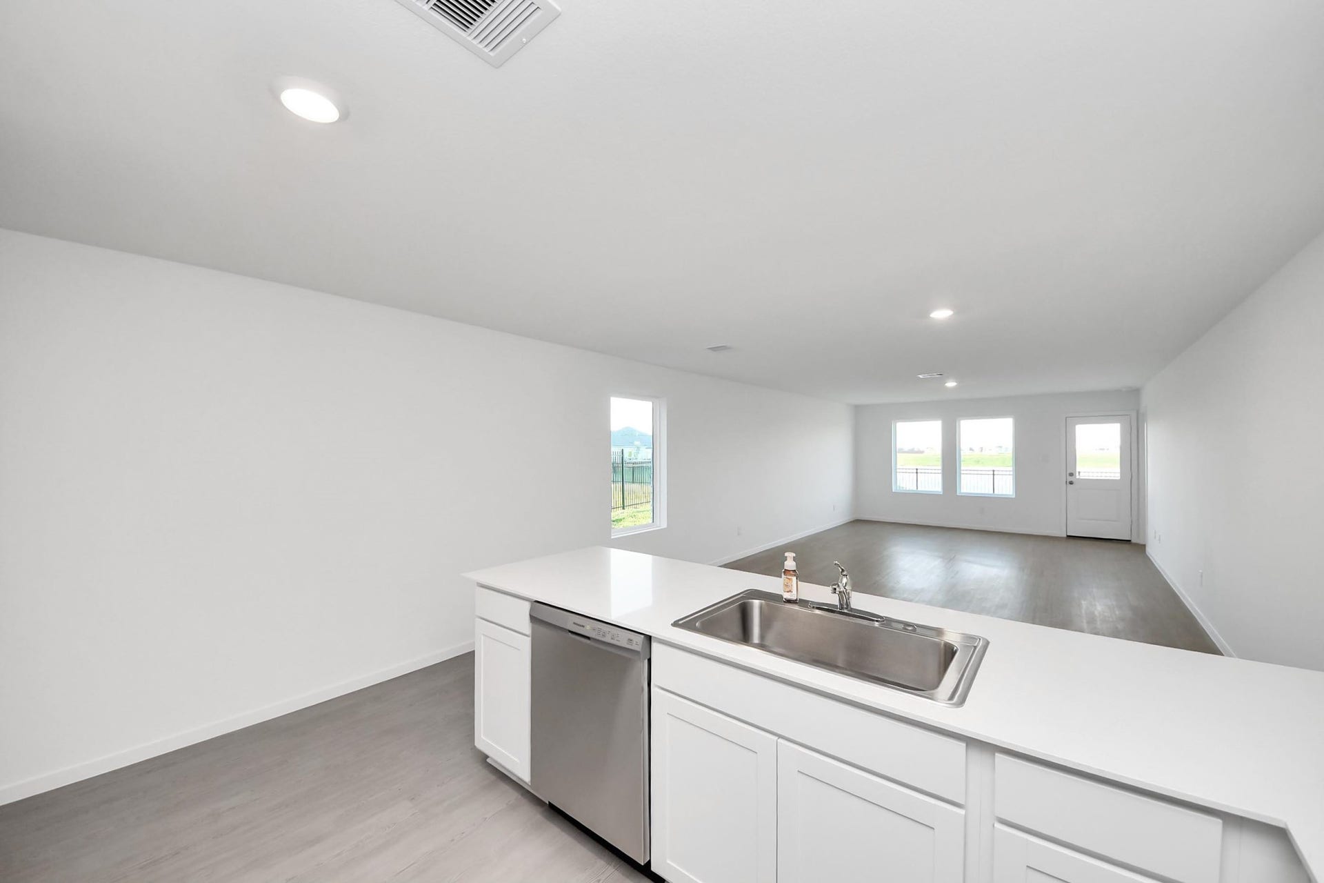 3096 Sunset Glory Drive, Katy, TX 77493 Bright, open-concept living space with modern kitchen featuring a stainless steel dishwasher and sink. Large windows and a glass door provide ample natural light and views of the outdoors.