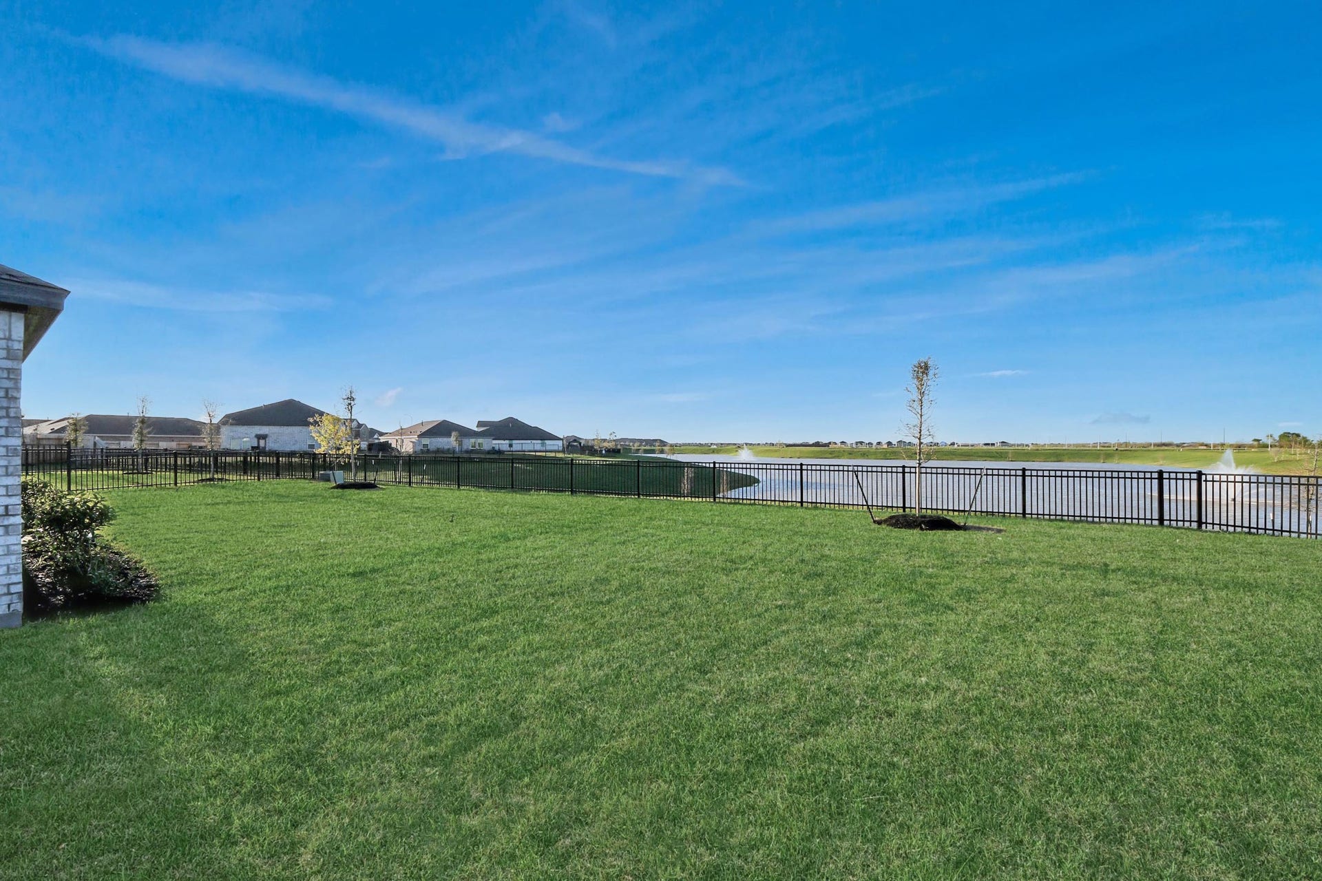 3096 Sunset Glory Drive, Katy, TX 77493 Spacious backyard with lush green lawn, enclosed by a fence, offering serene lake views and a clear blue sky. Ideal for outdoor relaxation or entertaining.